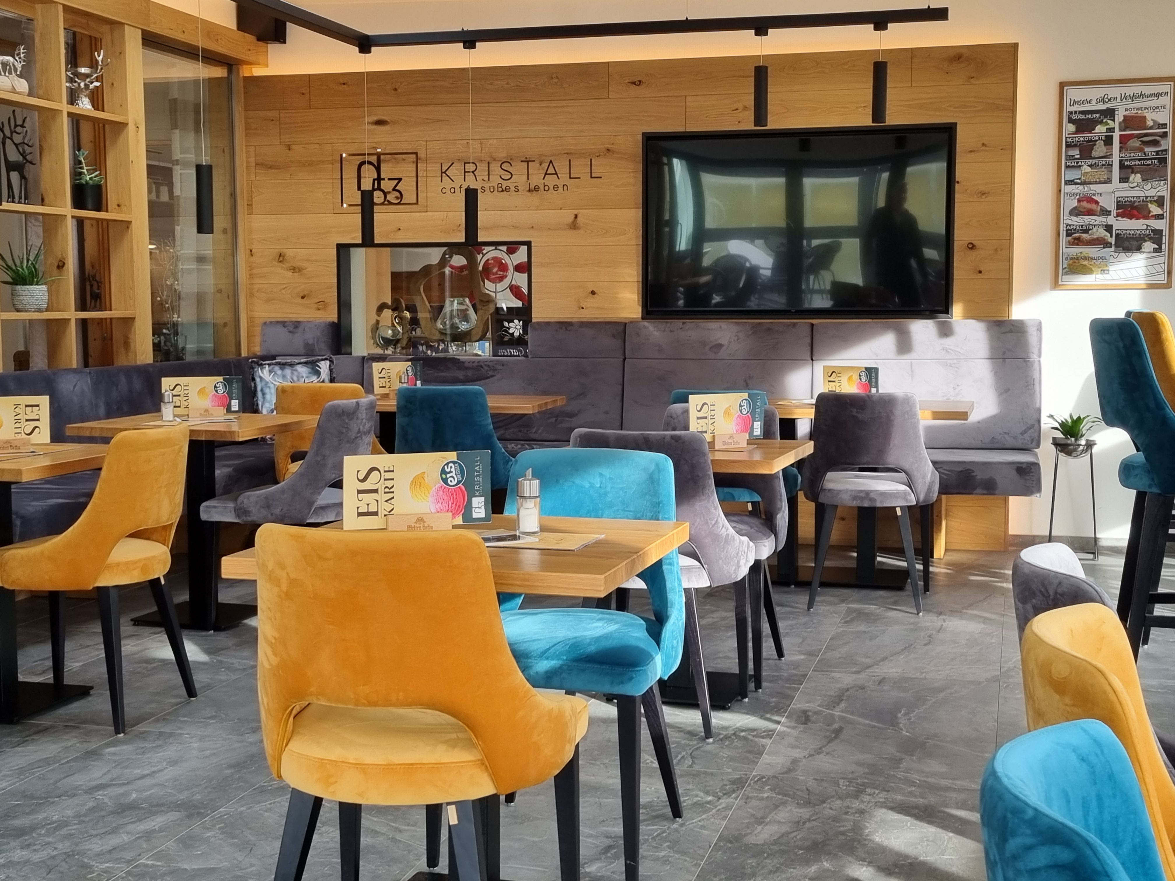 Pohľad do interiéru modernej kaviarne s farebnými zamatovými stoličkami a drevenými stenami.