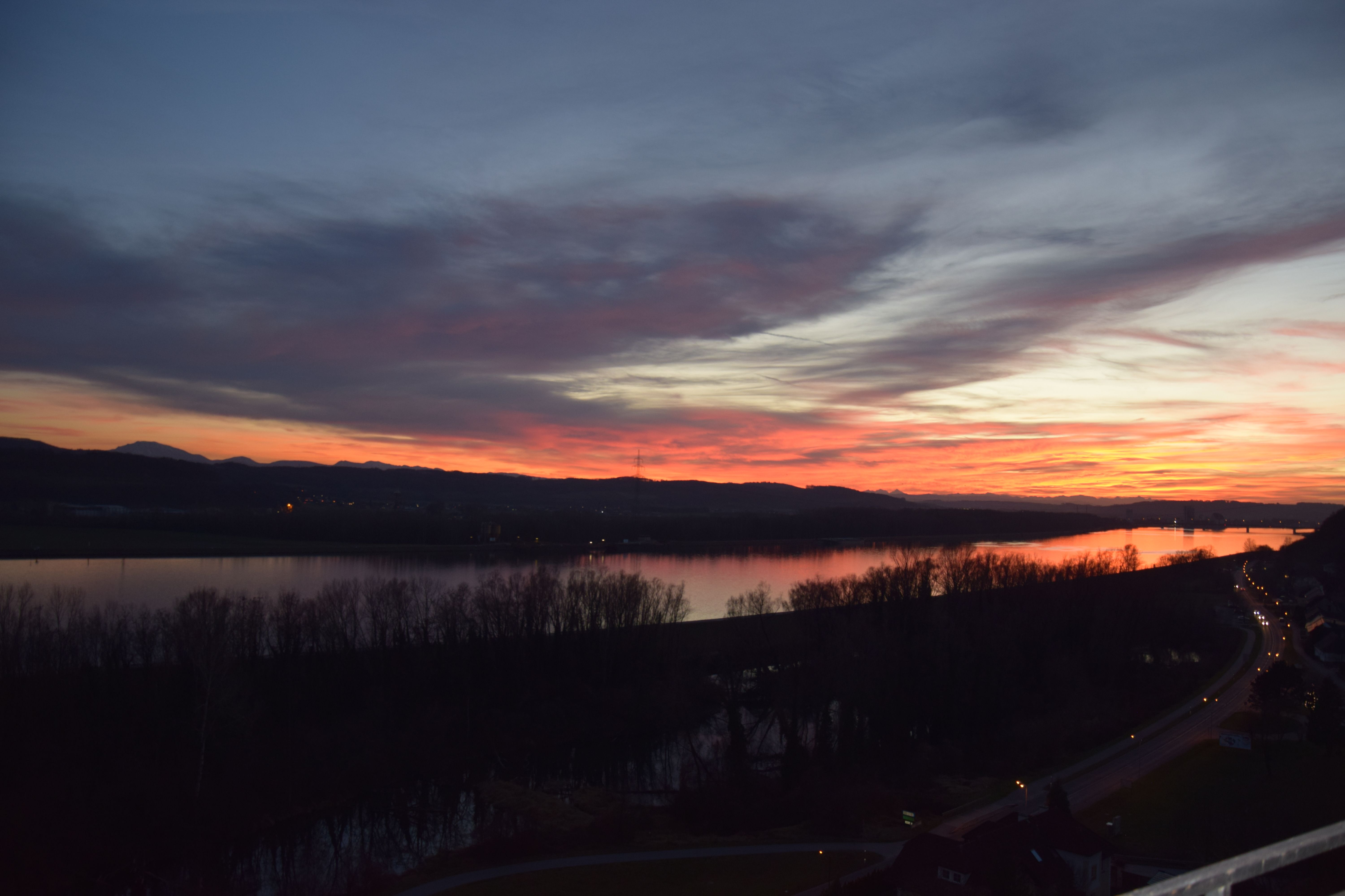 Západ slnka nad riekou so stromami a cestou v popredí.