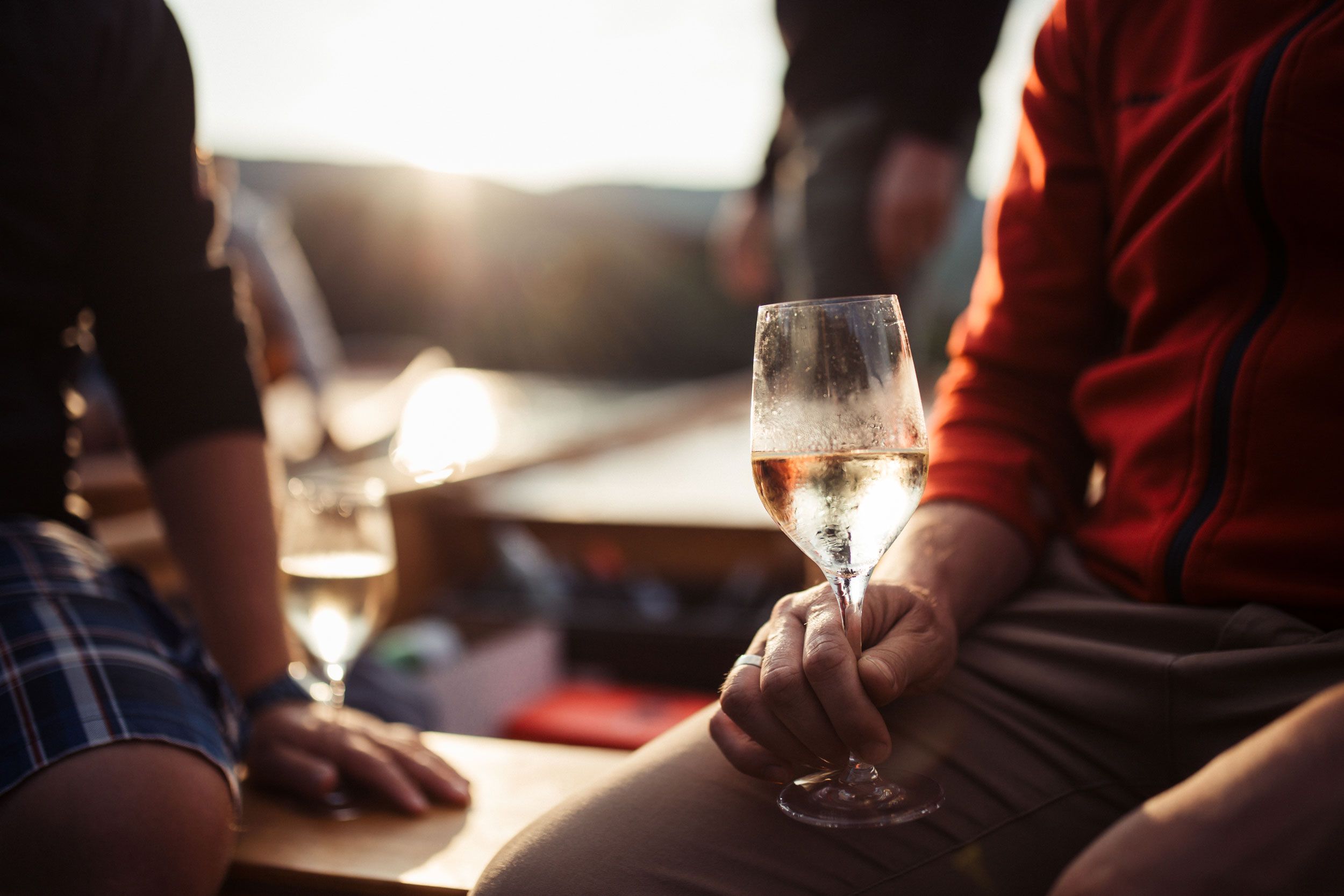 Osoba držiaca pohár s vínom, v pozadí západ slnka.