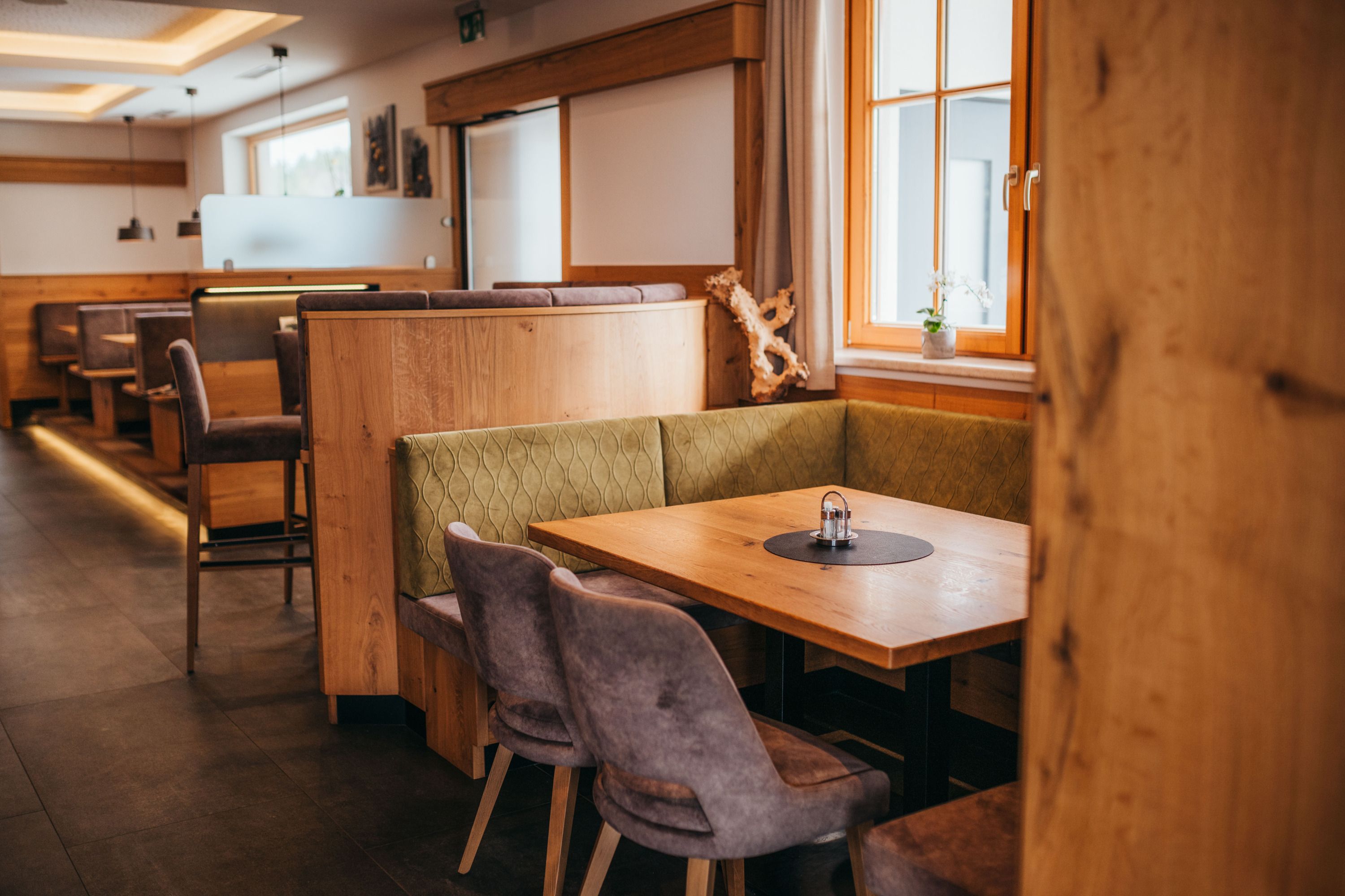 Útulná jedáleň s dreveným nábytkom a čalúnenými lavicami, okno so závesmi, stôl so soľničkami a koreničkami.