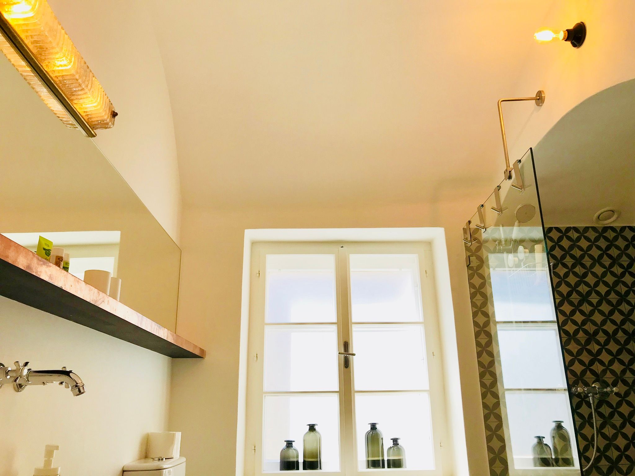 Moderná kúpeľňa so skleneným sprchovacím kútom a dekoratívnymi obkladmi.