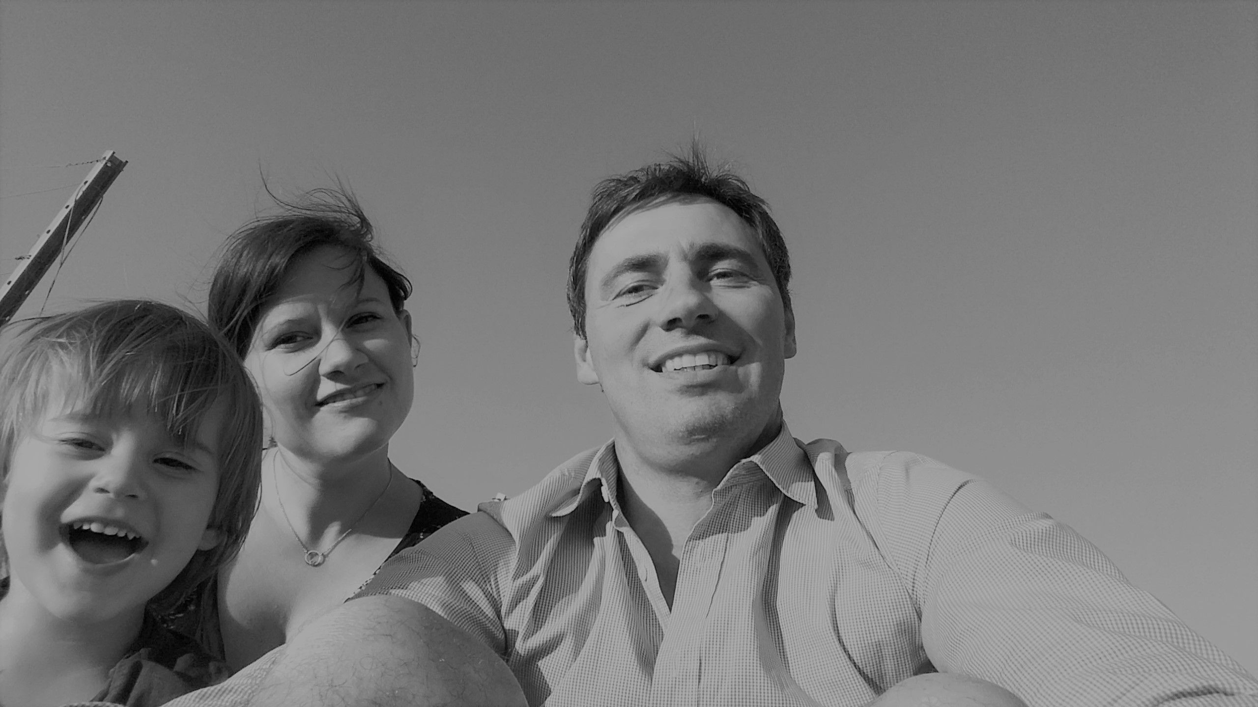 Čiernobiela fotografia usmievajúcej sa rodiny pozostávajúcej z muža, ženy a dieťaťa, ktorí sa pozerajú do fotoaparátu.