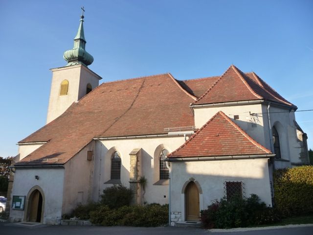 Historický kostol s červenou škridlovou strechou a malou vežou so zelenou strechou.