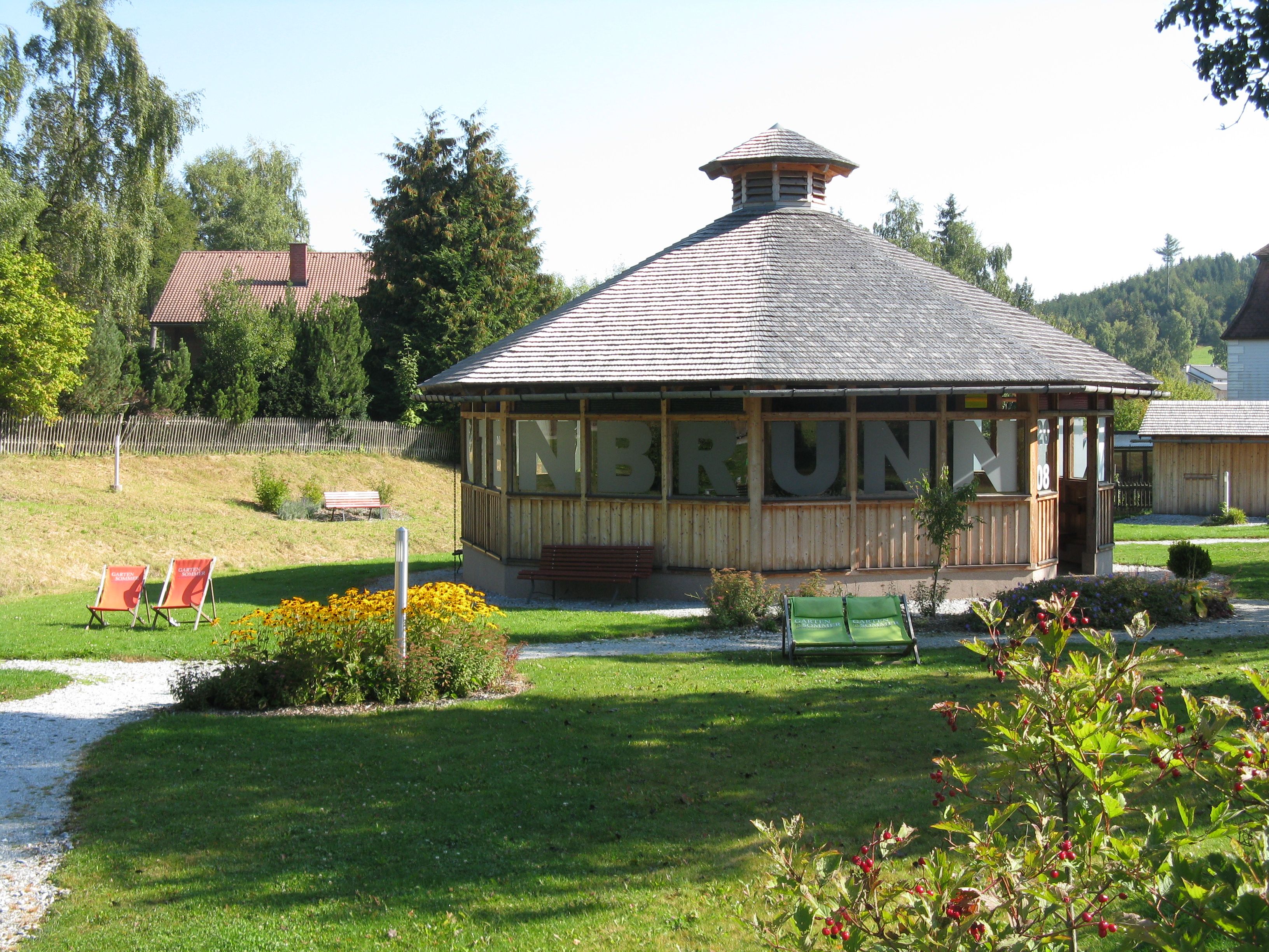 Pavilón v zelenom parku s kvetmi a ležadlami.