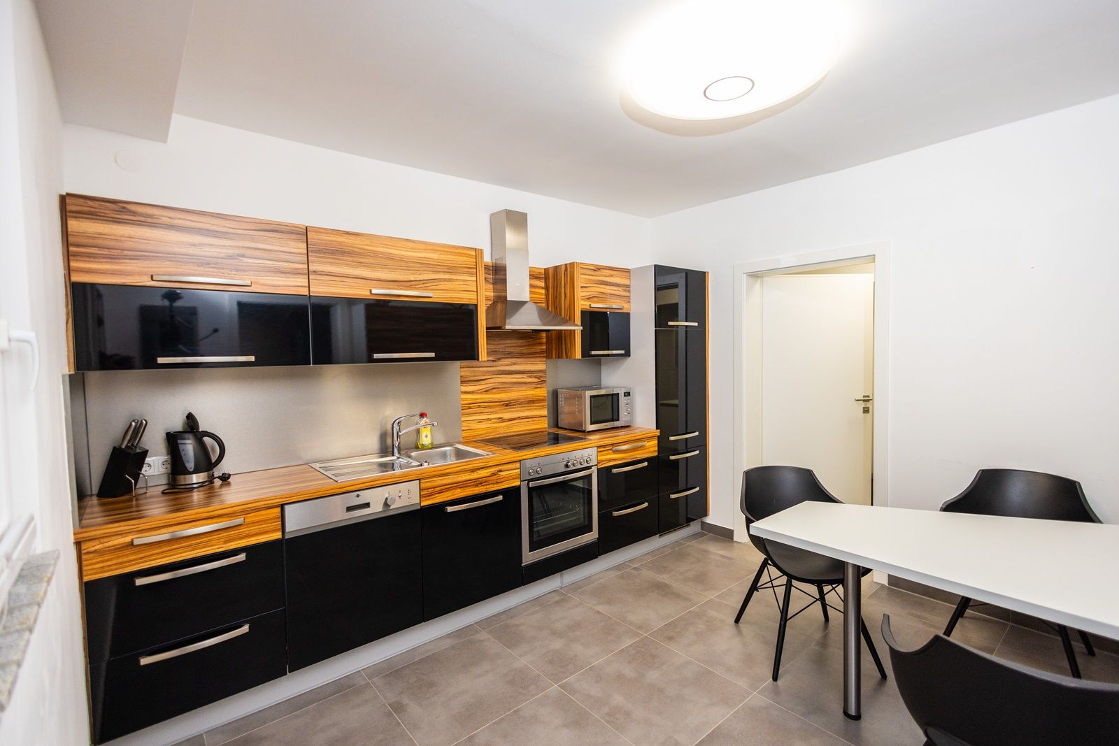 Moderná kuchyňa s drevenými a čiernymi lesklými prednými stenami, jedálenský stôl a stoličky.