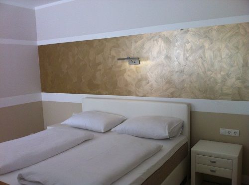 Moderná spálňa s manželskou posteľou a zlatou nástennou dekoráciou.