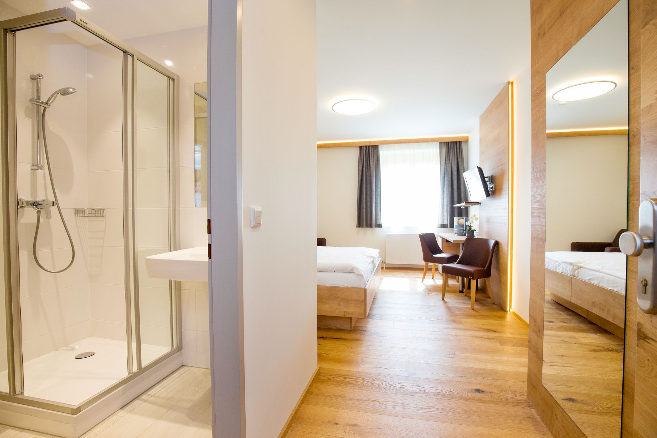 Moderná hotelová izba s kúpeľňou, posteľou, stolom a stoličkami.