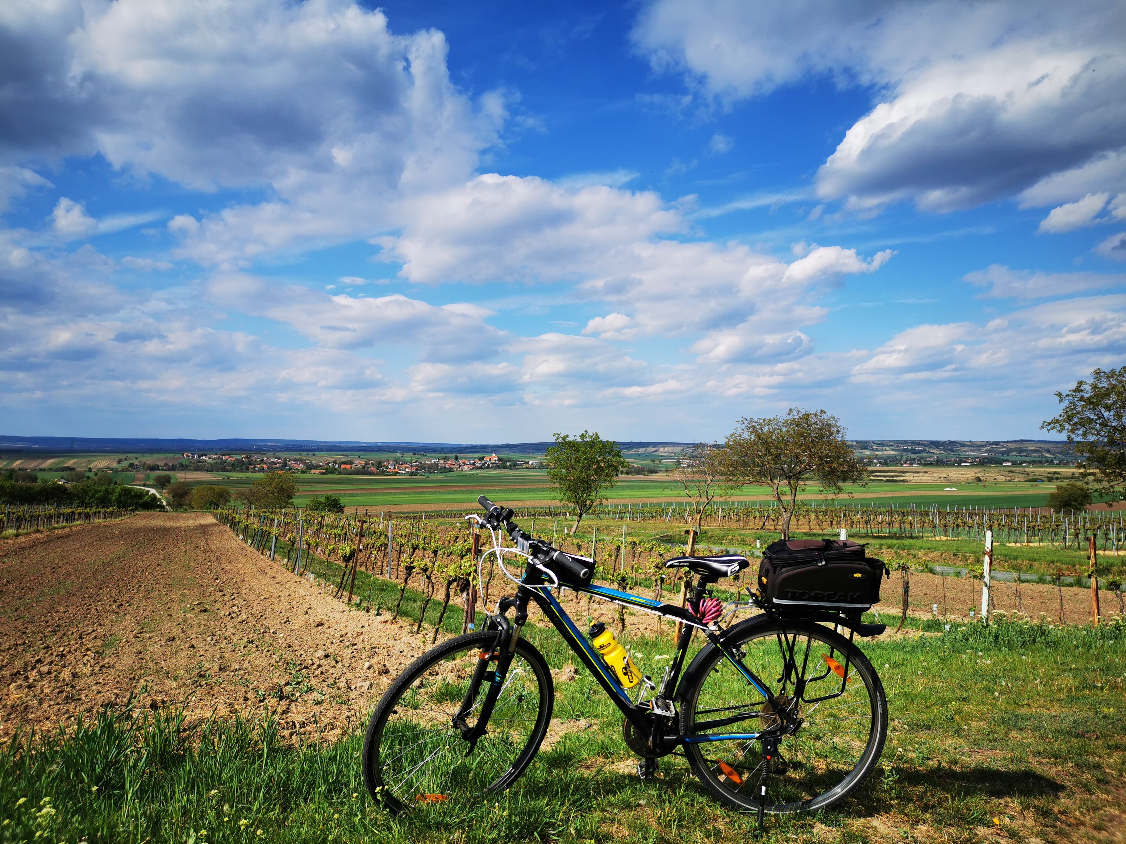 Bicykel pred krajinou s poliami a modrou oblohou.