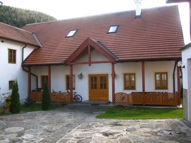 Tradičná budova s červenou škridlovou strechou a drevenými prvkami, obklopená vydláždeným nádvorím.