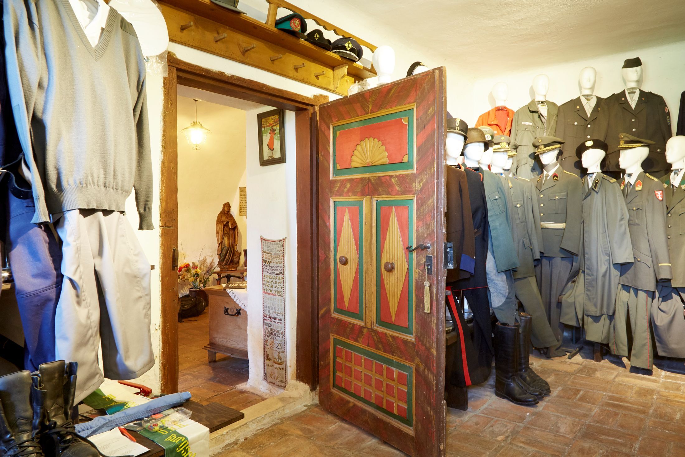 Pohľad do interiéru miestnosti so starými uniformami a farebne natretými drevenými dverami.