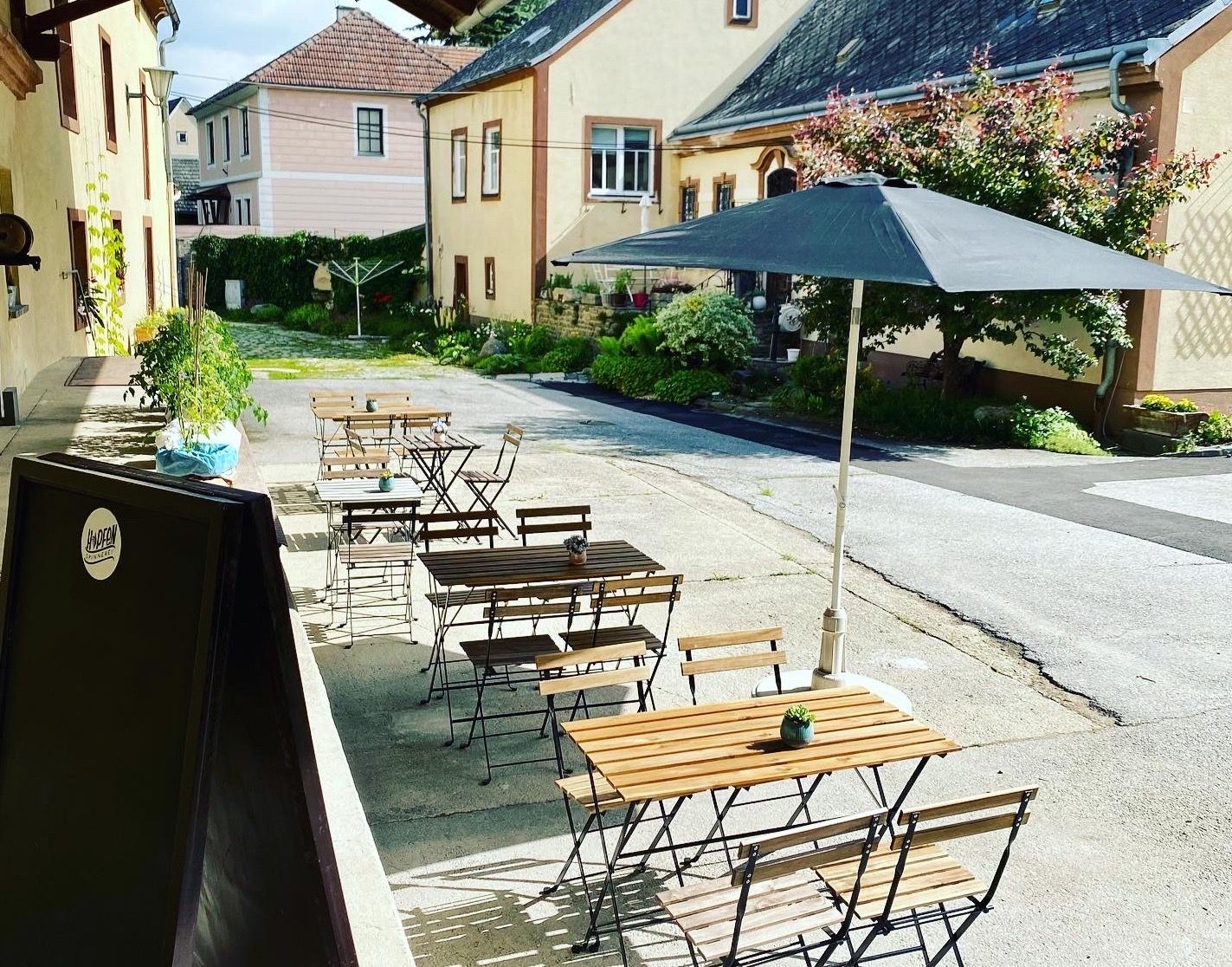 Záhrada pre hostí s drevenými stolmi a stoličkami, slnečníkom a rastlinami vo vnútornom dvore.