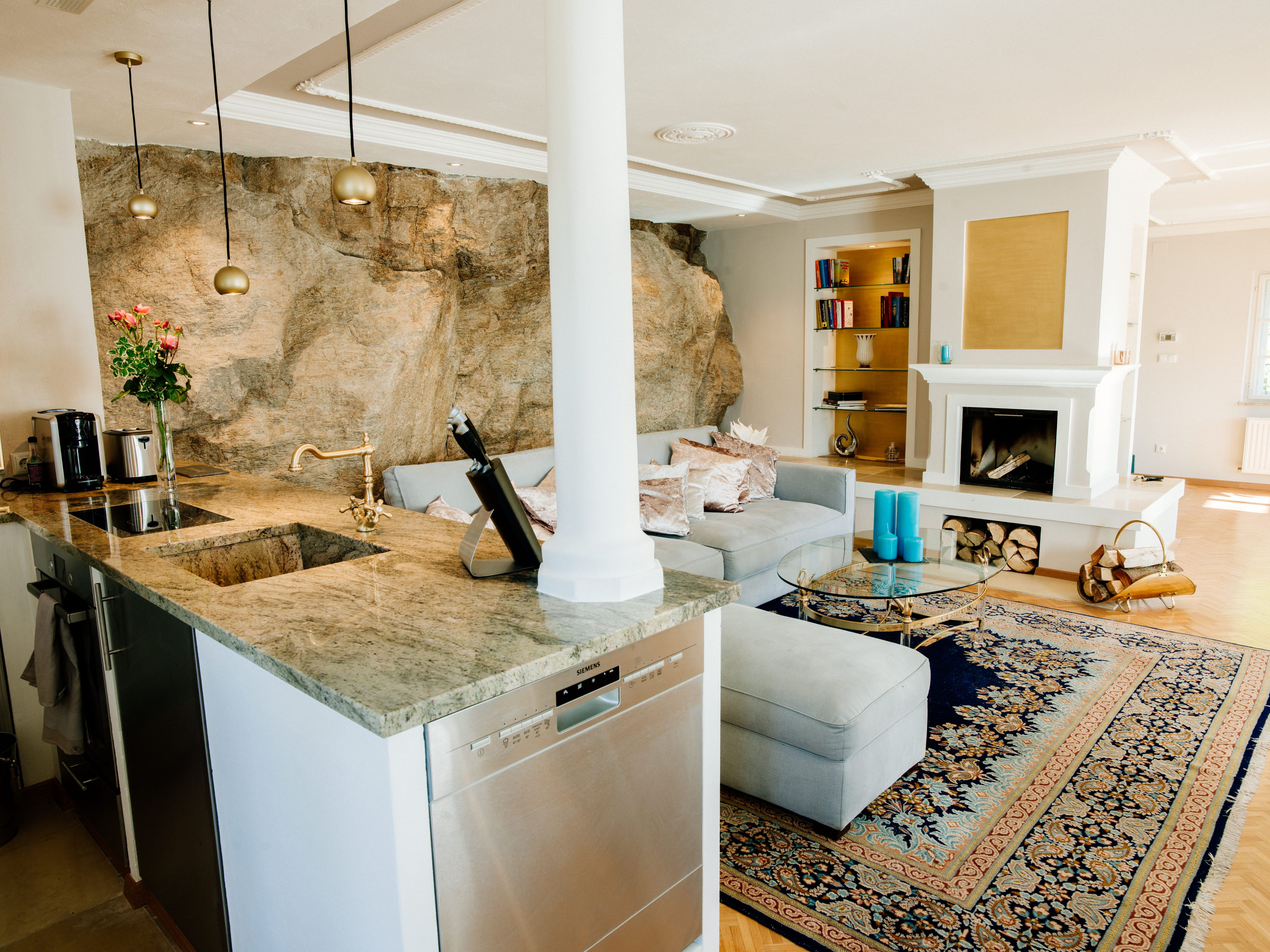 Elegantná obývacia izba s krbom, kobercom a otvorenou kuchyňou.