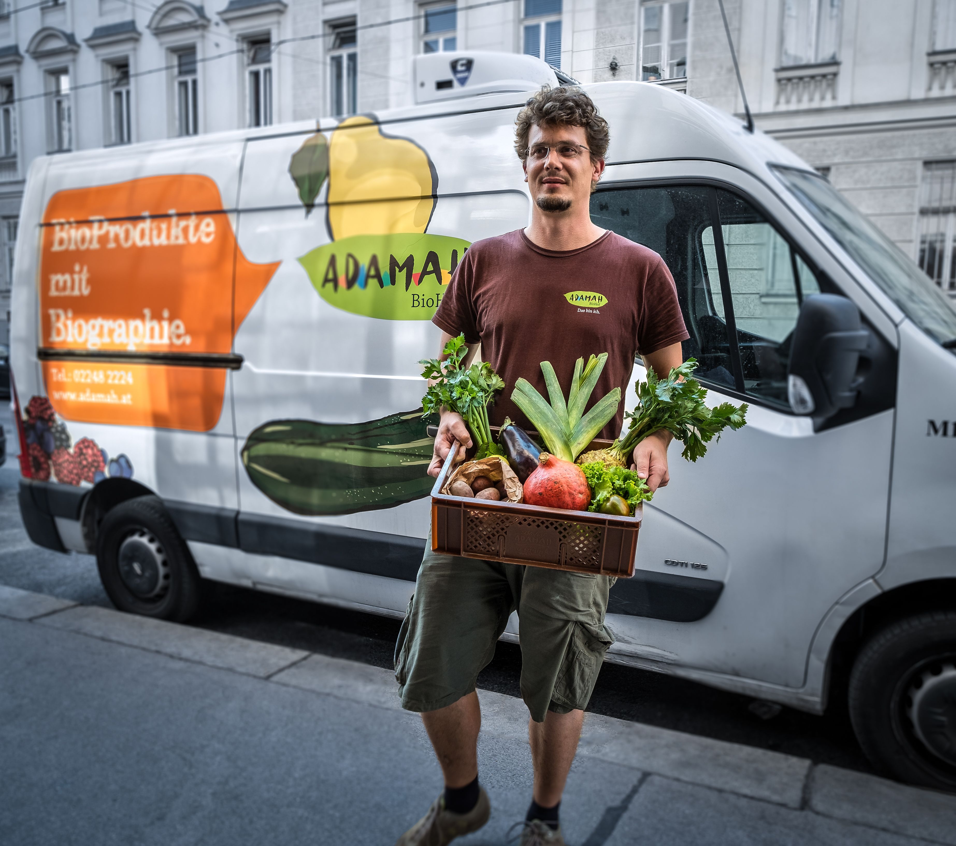 Muž drží škatuľu s čerstvým ovocím a zeleninou pred dodávkou s logom ADAMAH.
