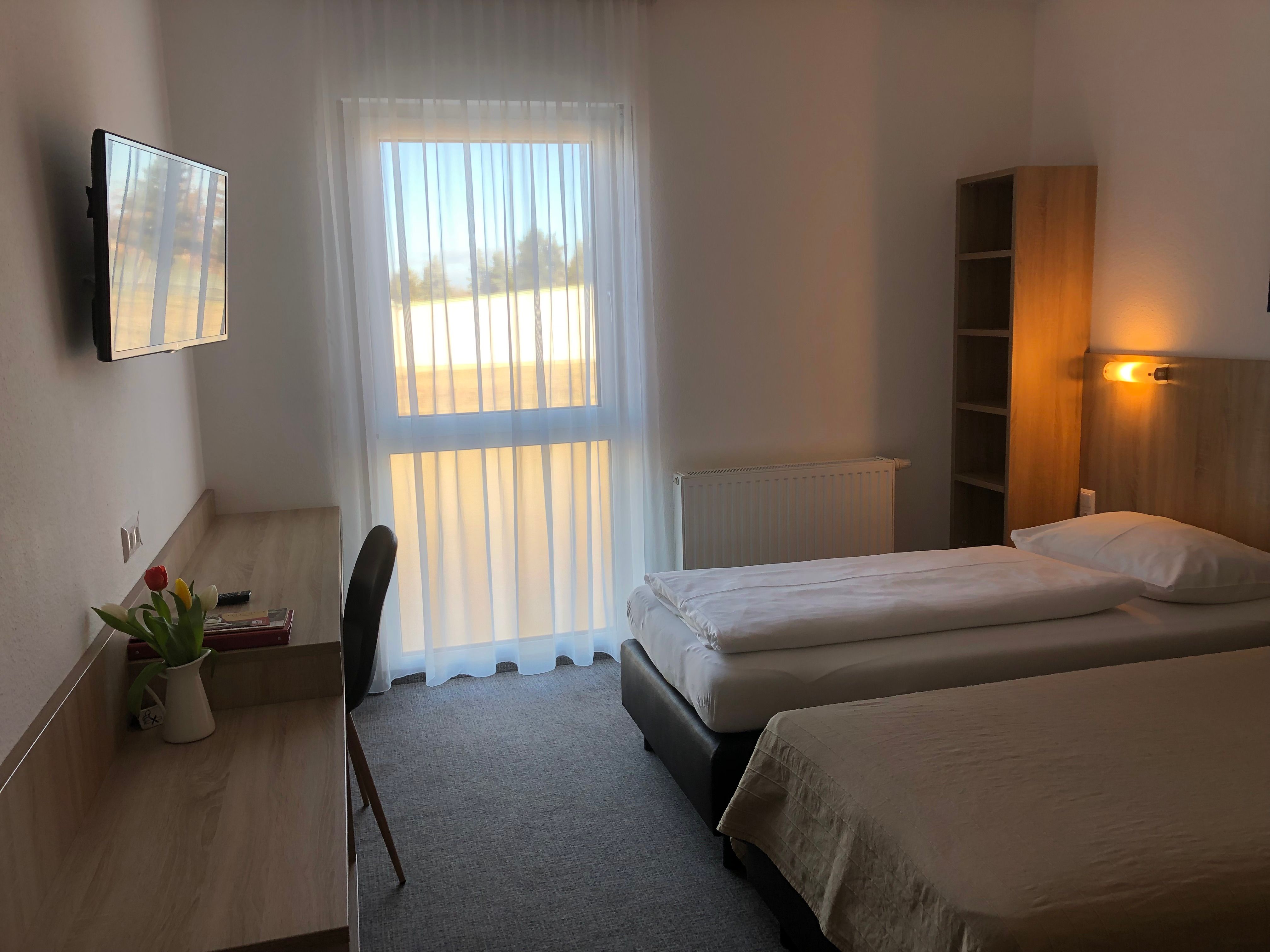 Jednoducho zariadená motelová izba s dvoma samostatnými posteľami, písacím stolom, televízorom a oknom so závesmi.