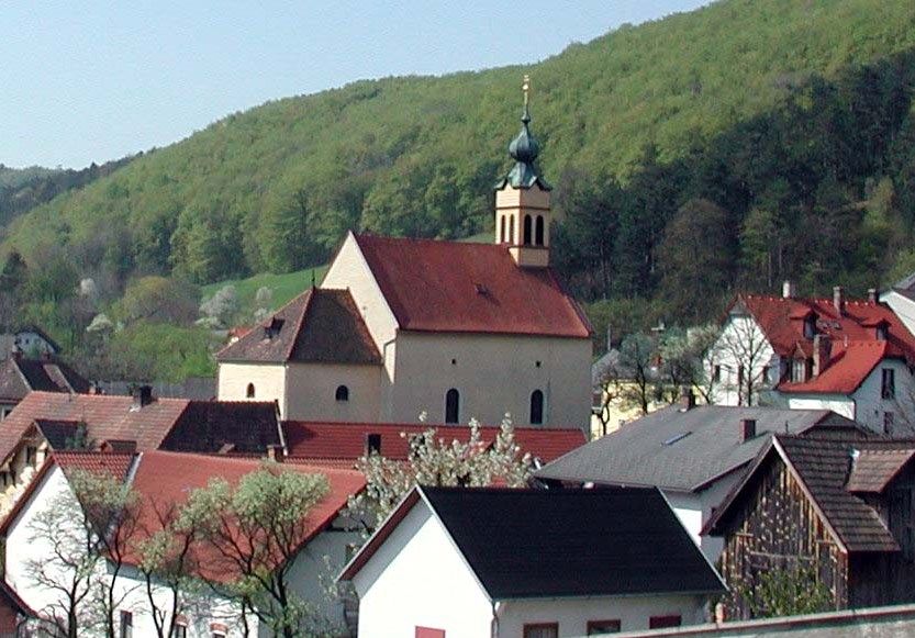 Pútnický kostol Maria Raisenmarkt vo vidieckom prostredí s kopcami v pozadí.
