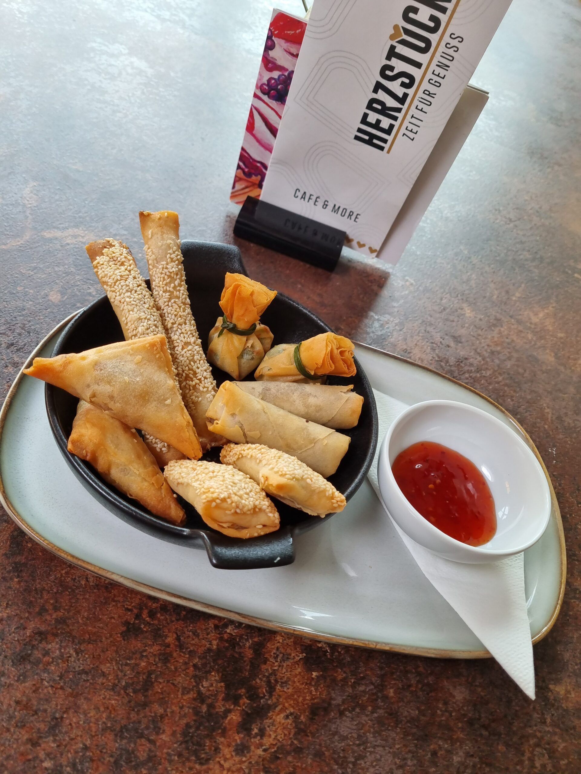 Rôzne vyprážané občerstvenie na tanieri s dipom a kaviarenským menu v pozadí.