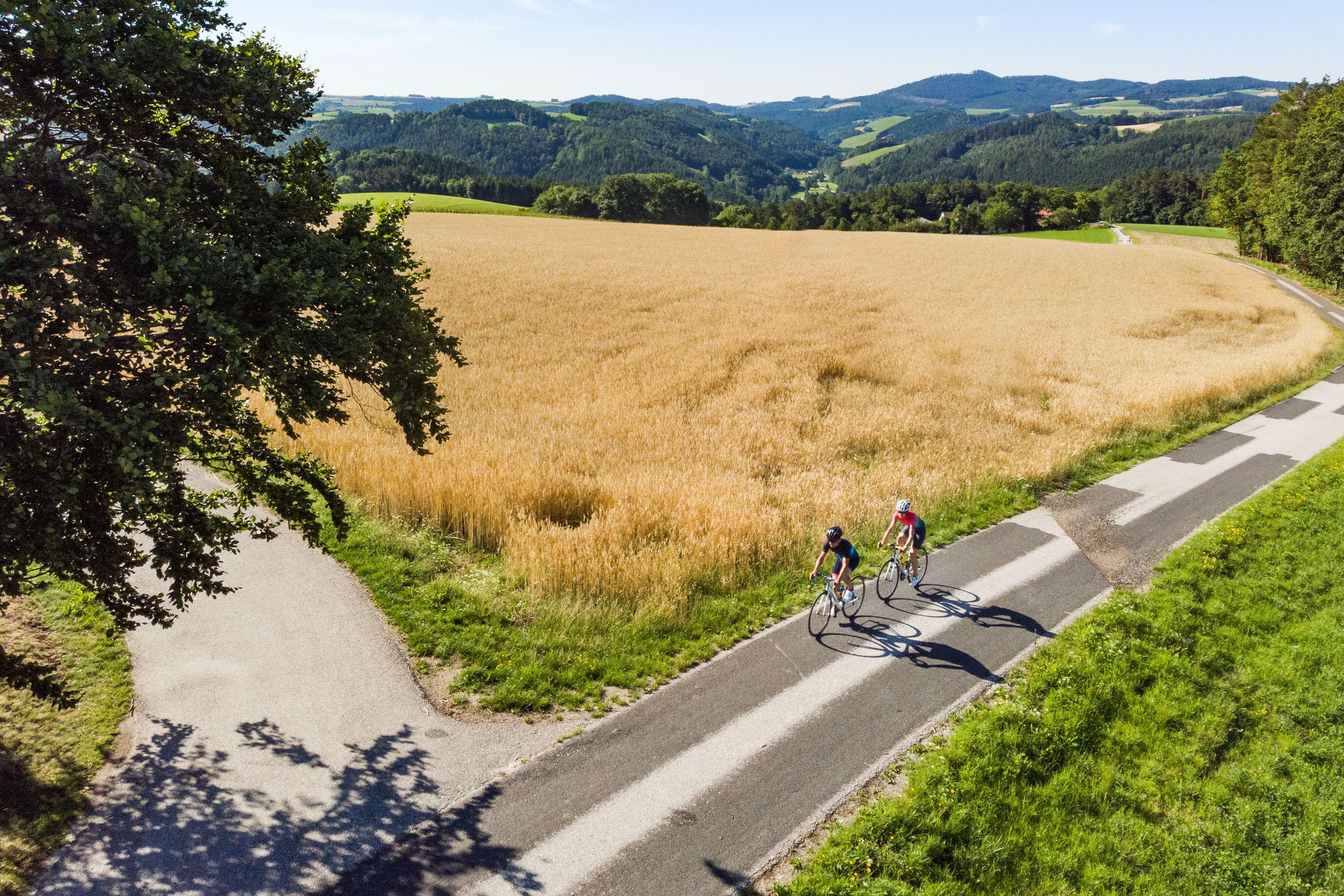 Letecký pohľad na dvoch ľudí na pretekárskych bicykloch vedľa poľa, v pozadí kopce