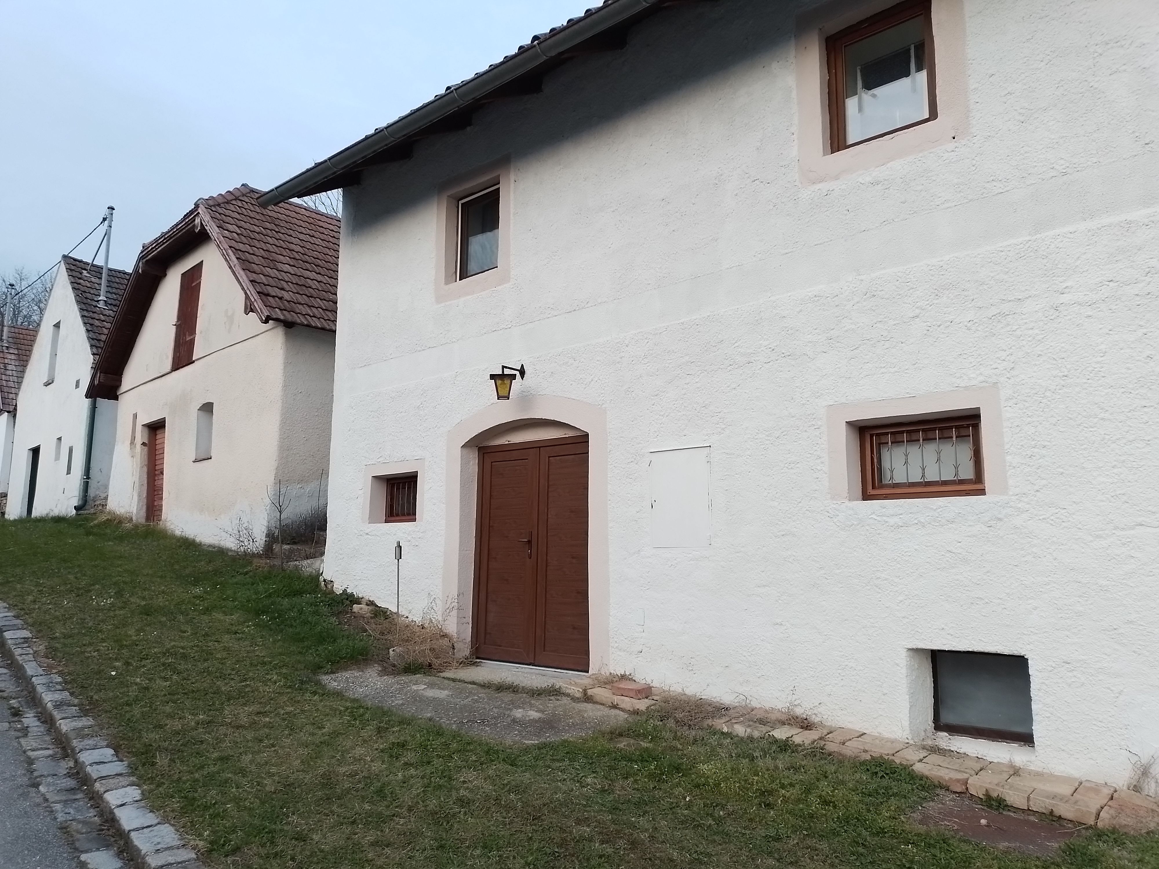 Rad bielych domov s hnedými dverami a oknami pozdĺž cesty s trávnatými okrajmi.