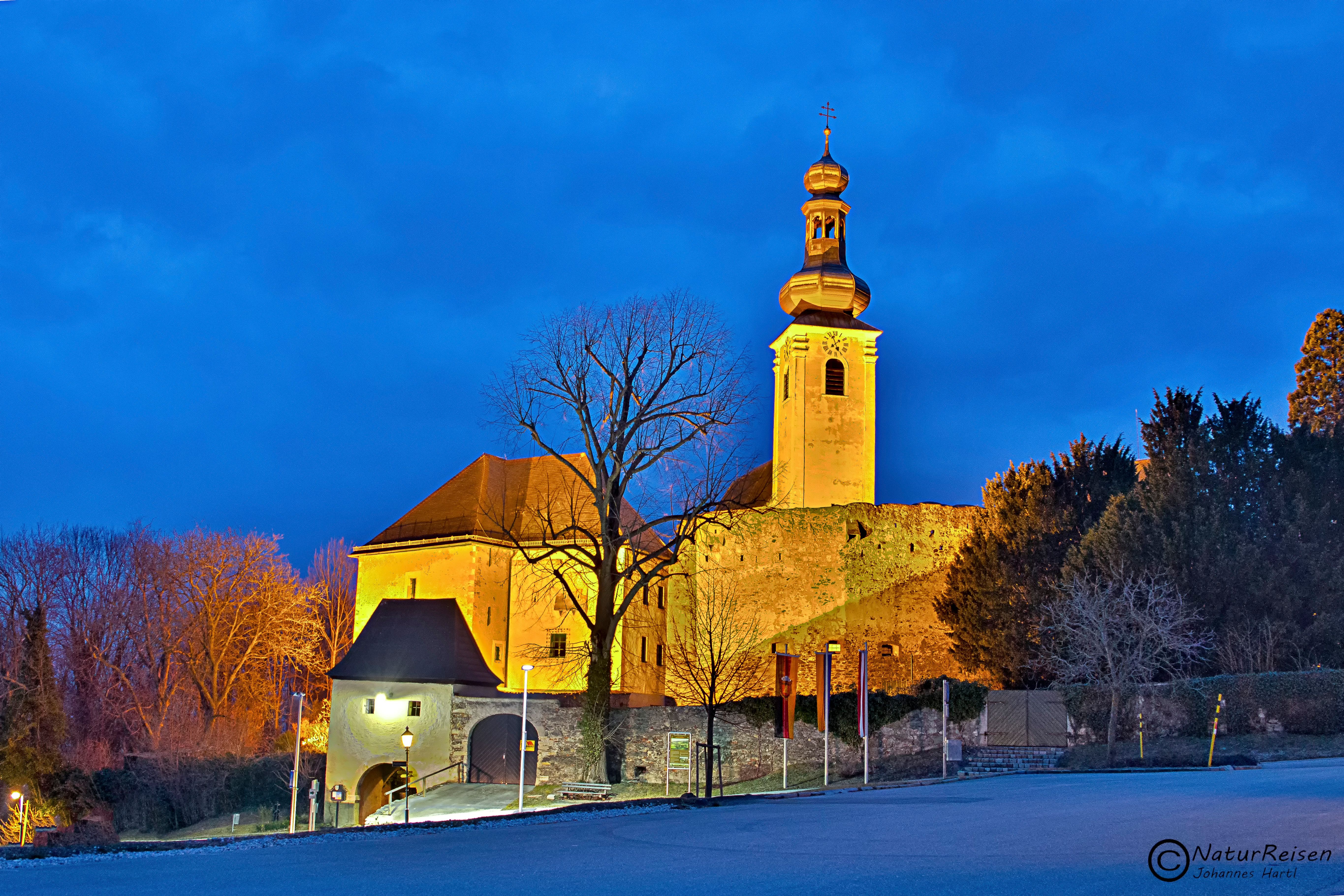 Osvetlený hrad Gloggnitz za súmraku s modrou oblohou.