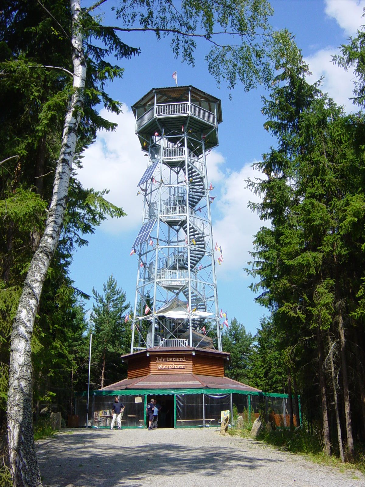 Vysoká kovová rozhľadňa s dreveným obložením, obklopená stromami, pod modrou oblohou.