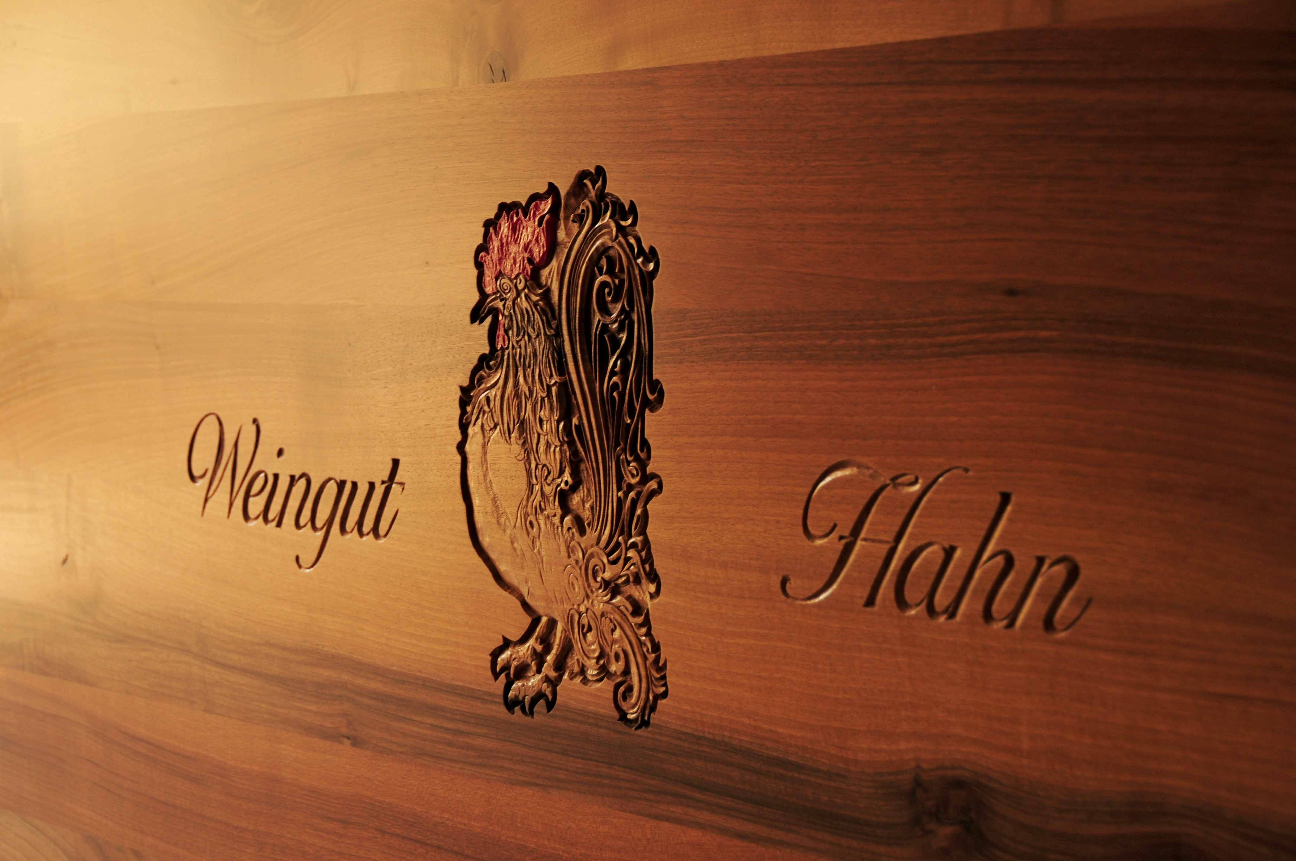 Drevený panel s vyrytým kohútom a nápisom "Weingut Hahn".