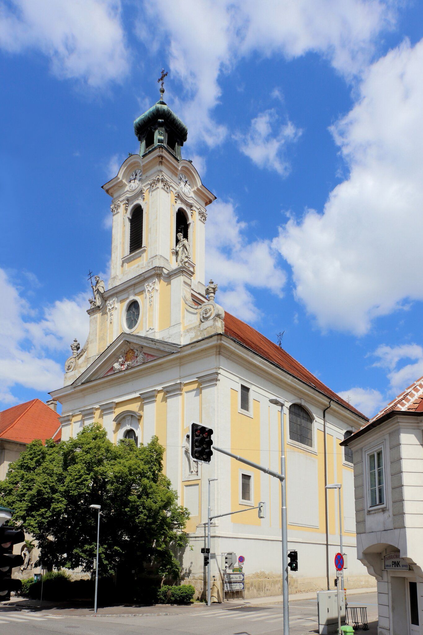 Barokový kostol s vežou a hodinami na pozadí modrej oblohy.