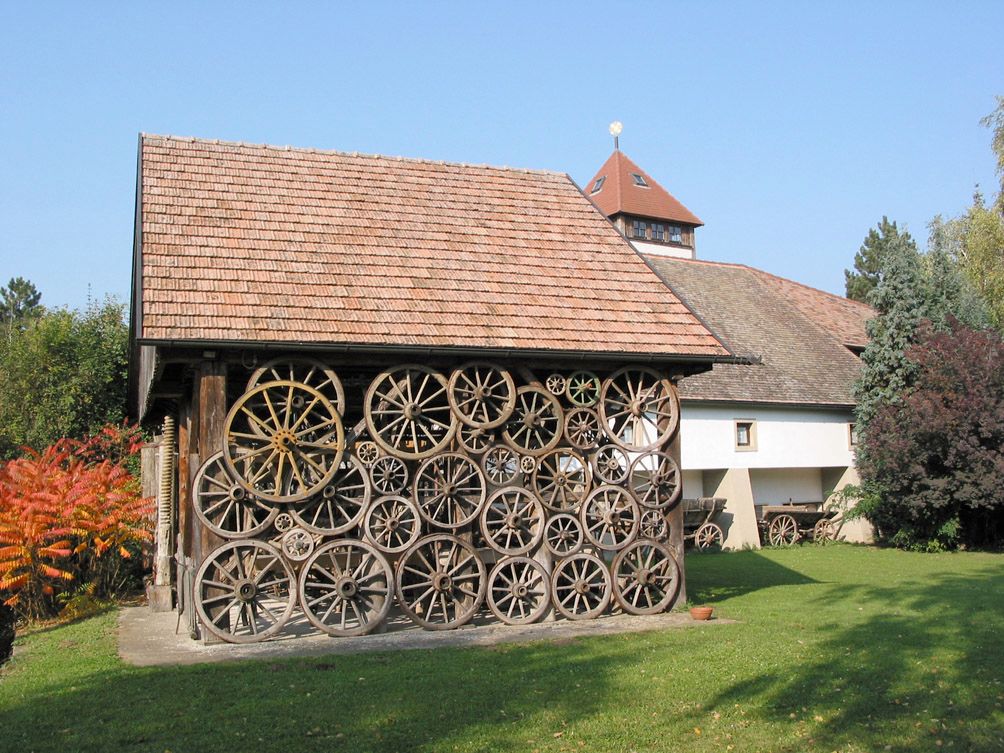 Budova s fasádou zo starých kolies voza, obklopená stromami a trávnikom.