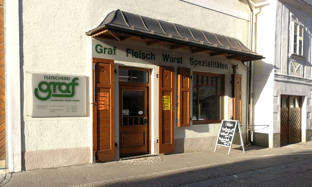Exteriérový pohľad na mäsiarstvo Graf s drevenými dverami a reklamnou tabuľou.