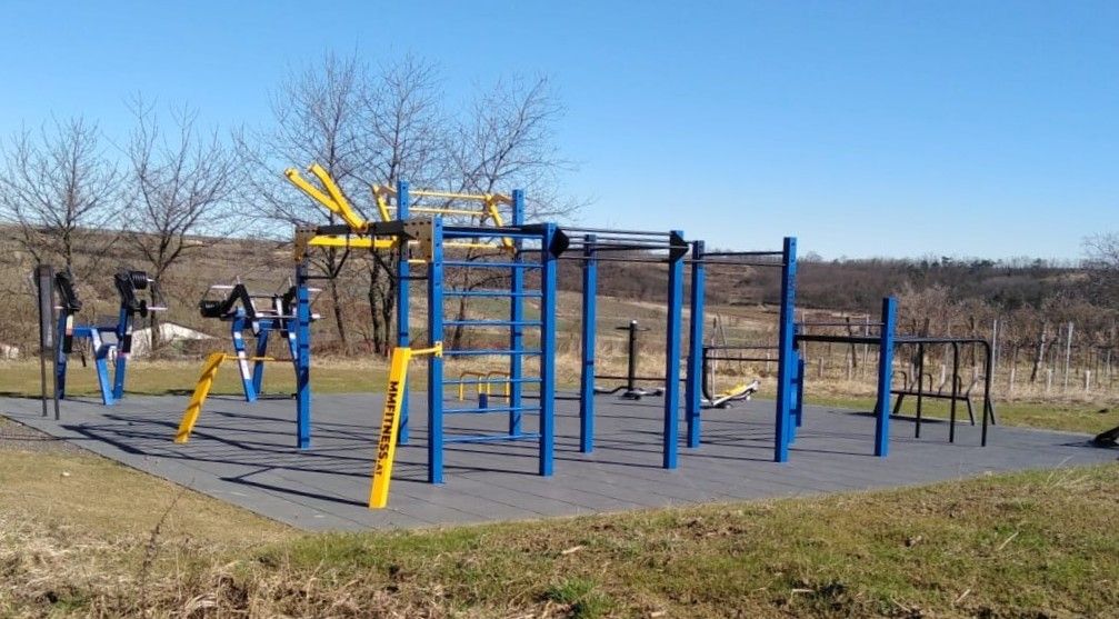 Vonkajší park na kalisteniku s modrými a žltými zariadeniami, obklopený vidieckou krajinou.