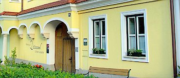 Žltá budova s bielymi okennými rámami a drevenými dverami.