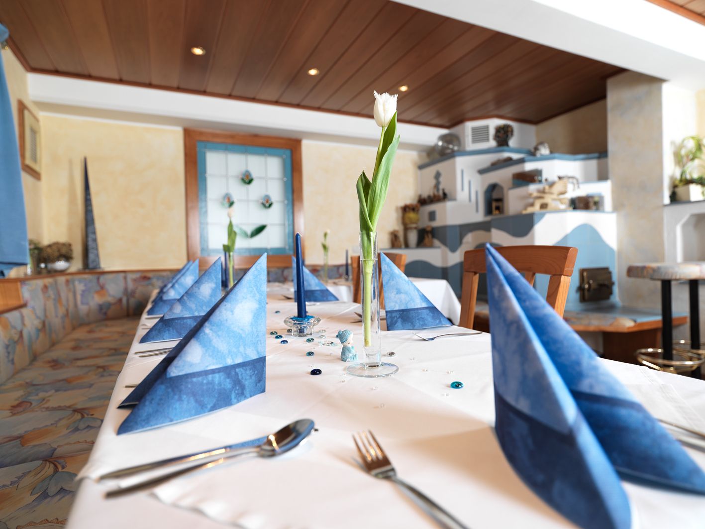Elegantne prestretý stôl s modrými obrúskami a bielym tulipánom v pohári v útulnej miestnosti.