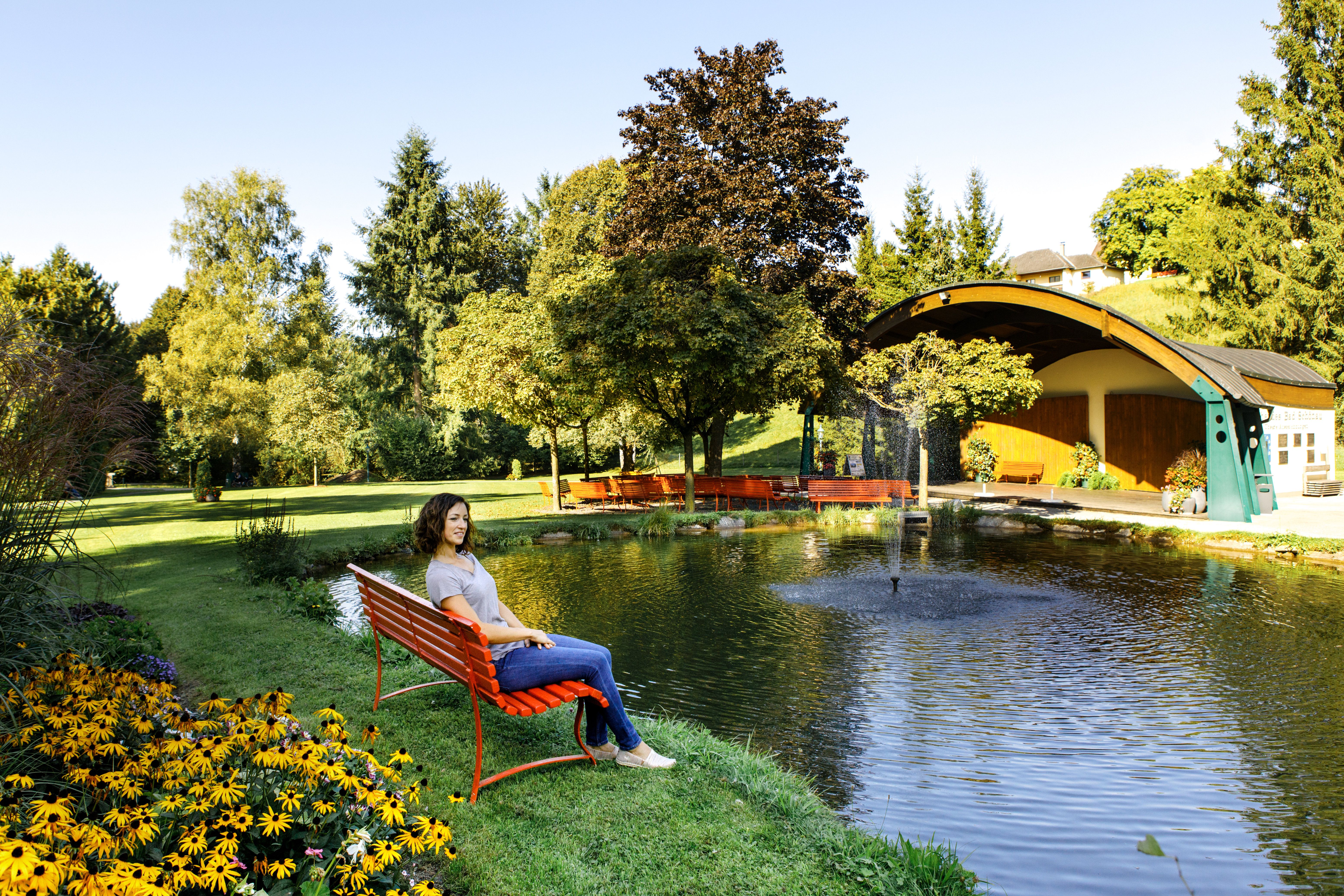 Žena sedí na červenej lavičke pri jazierku v kúpeľných záhradách Bad Schönau.