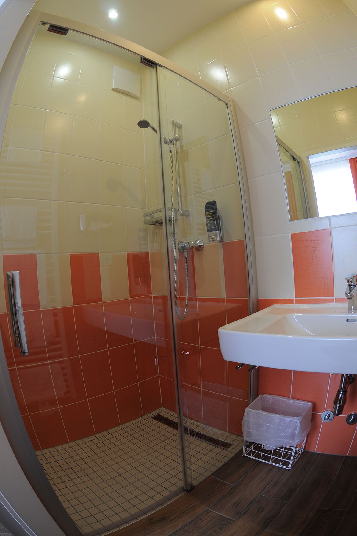 Kúpeľňa so sprchovacím kútom, umývadlom a oranžovo-bielymi dlaždicami.