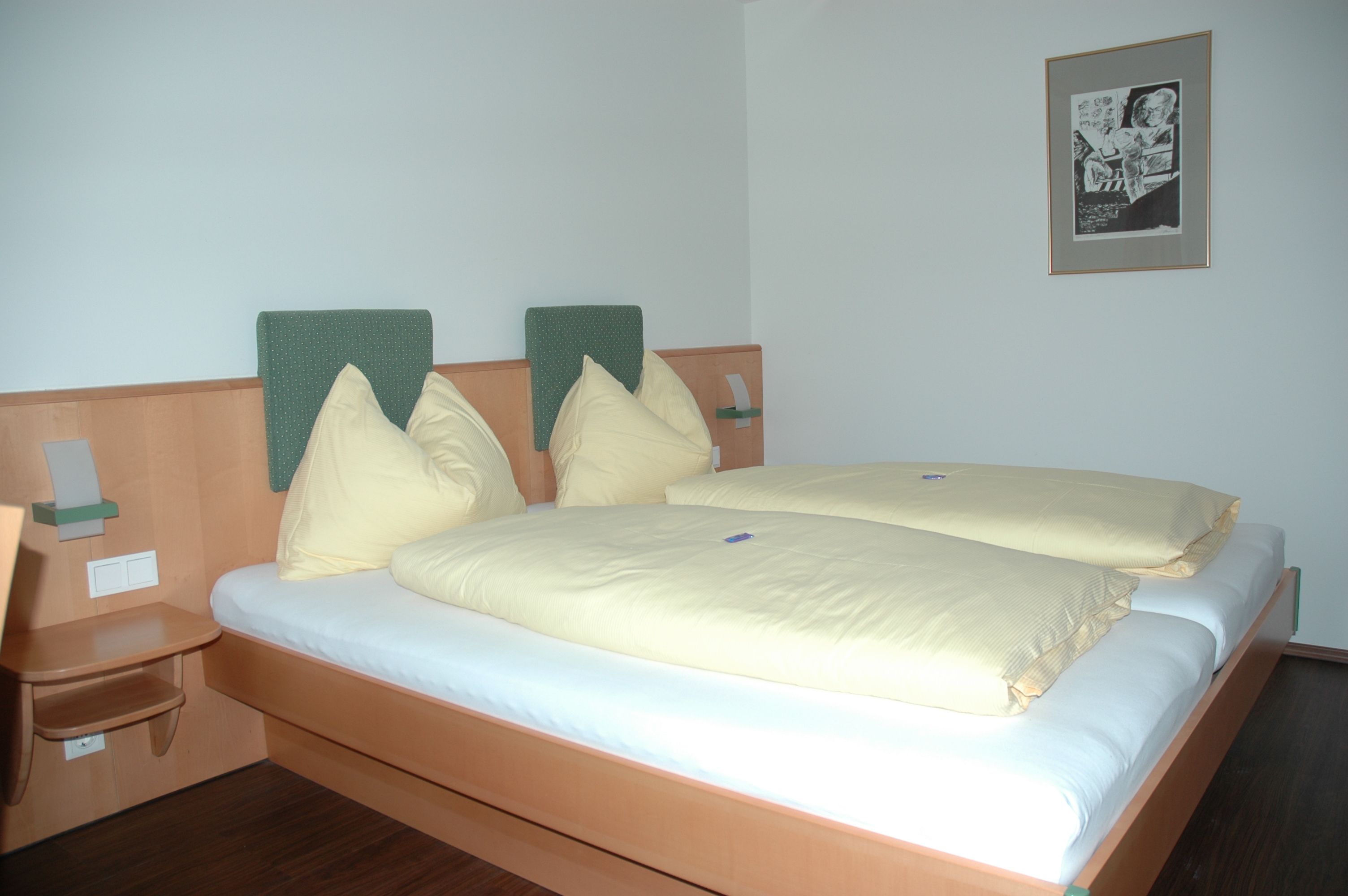 Hotelová izba s manželskou posteľou, žltou posteľnou bielizňou a nástennou maľbou.