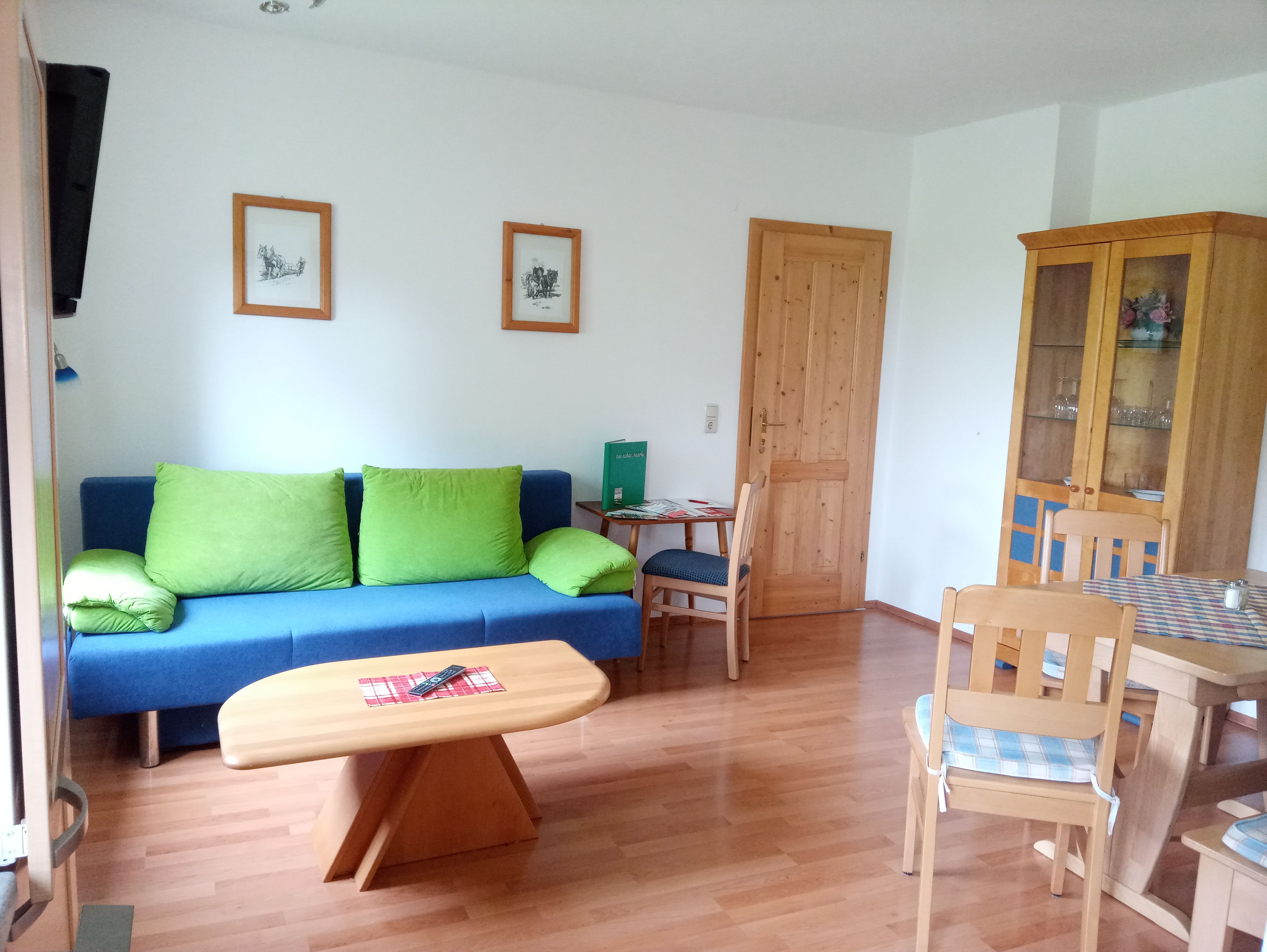 Obývacia izba s modrou pohovkou, dreveným stolom a stoličkami, šatníkovou skriňou a obrazmi na stene.