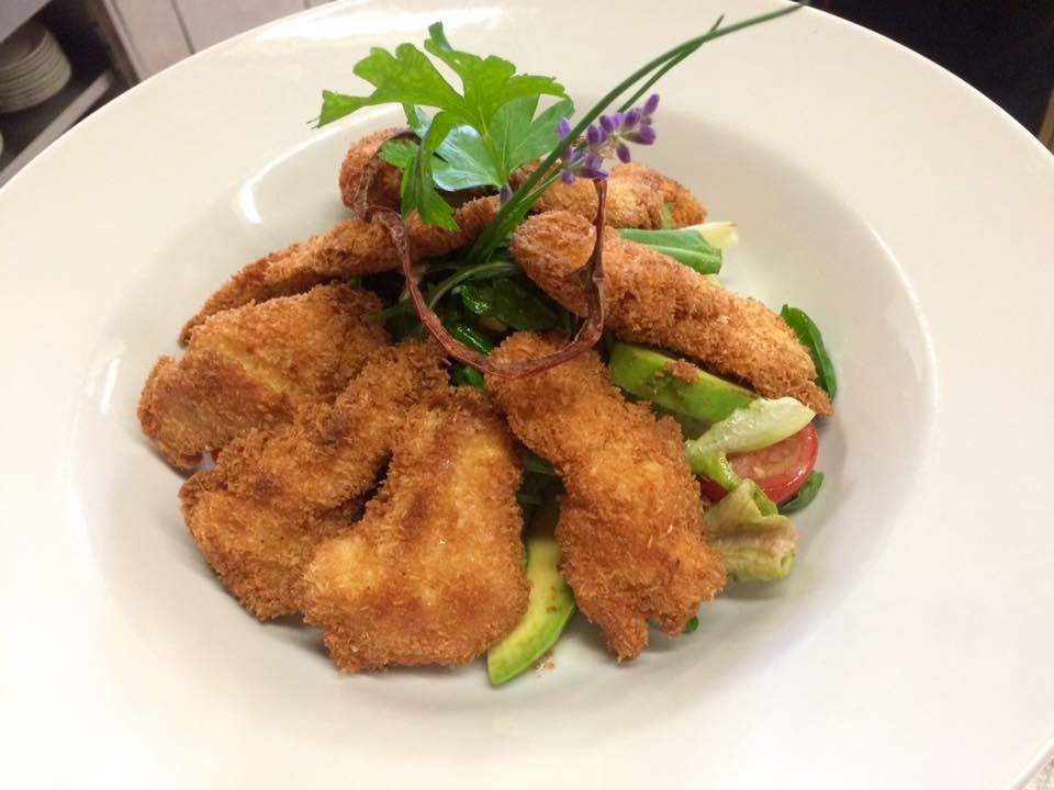 Tanier so šalátom a vyprážaným jedlom, ozdobený bylinkami.