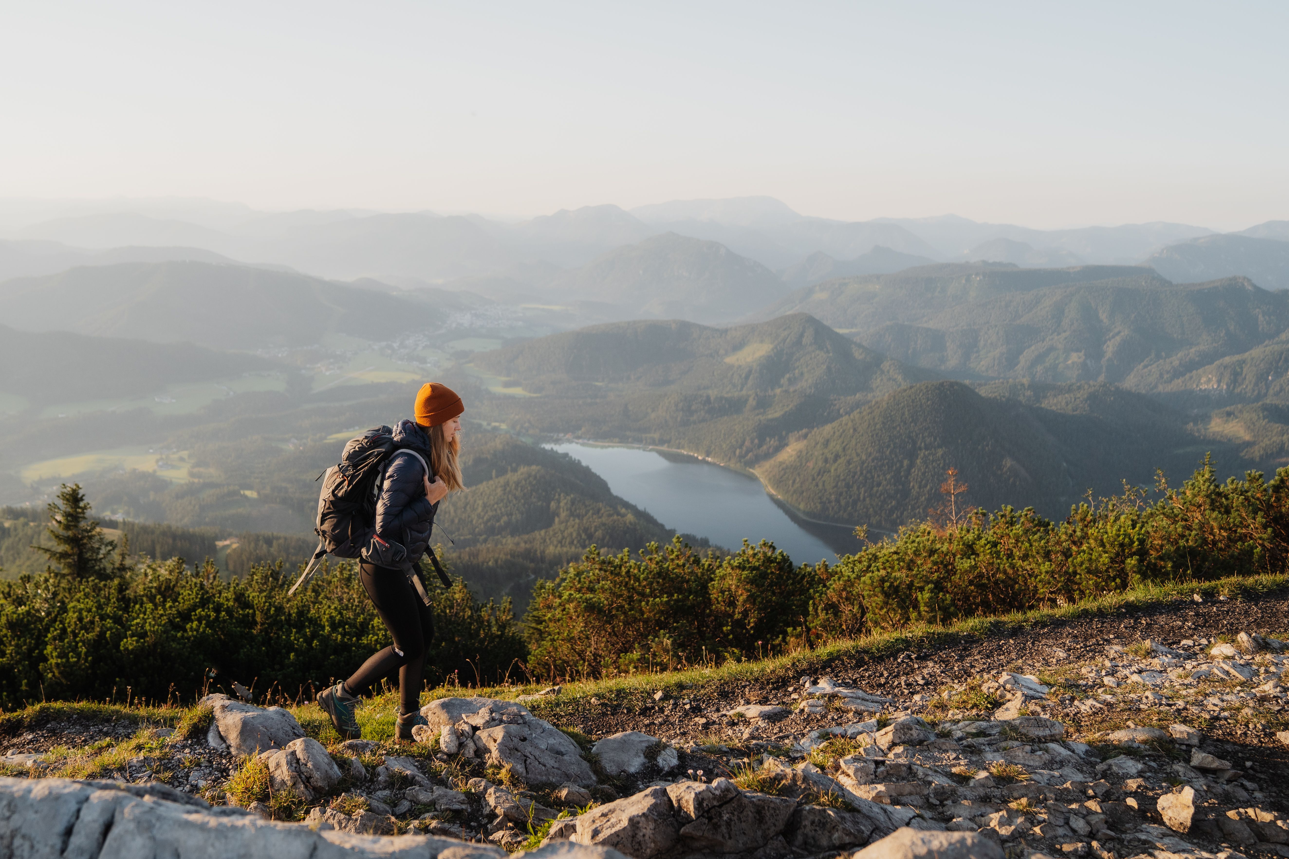 Die sanften Hügel und majestätischen Berge laden zu einem unvergesslichen Abenteuer ein. Ein Wanderer genießt die frische Bergluft und den atemberaubenden Blick auf den glitzernden See, während die Sonne sanft über die Landschaft strahlt.