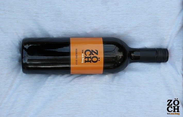 Fľaša vína s etiketou značky Zöch oranžovej farby na svetlom pozadí.