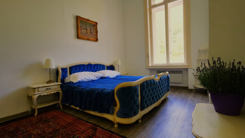 Elegantn&aacute; sp&aacute;lňa s modrou posteľou, starožitn&yacute;m n&aacute;bytkom a veľk&yacute;m oknom.