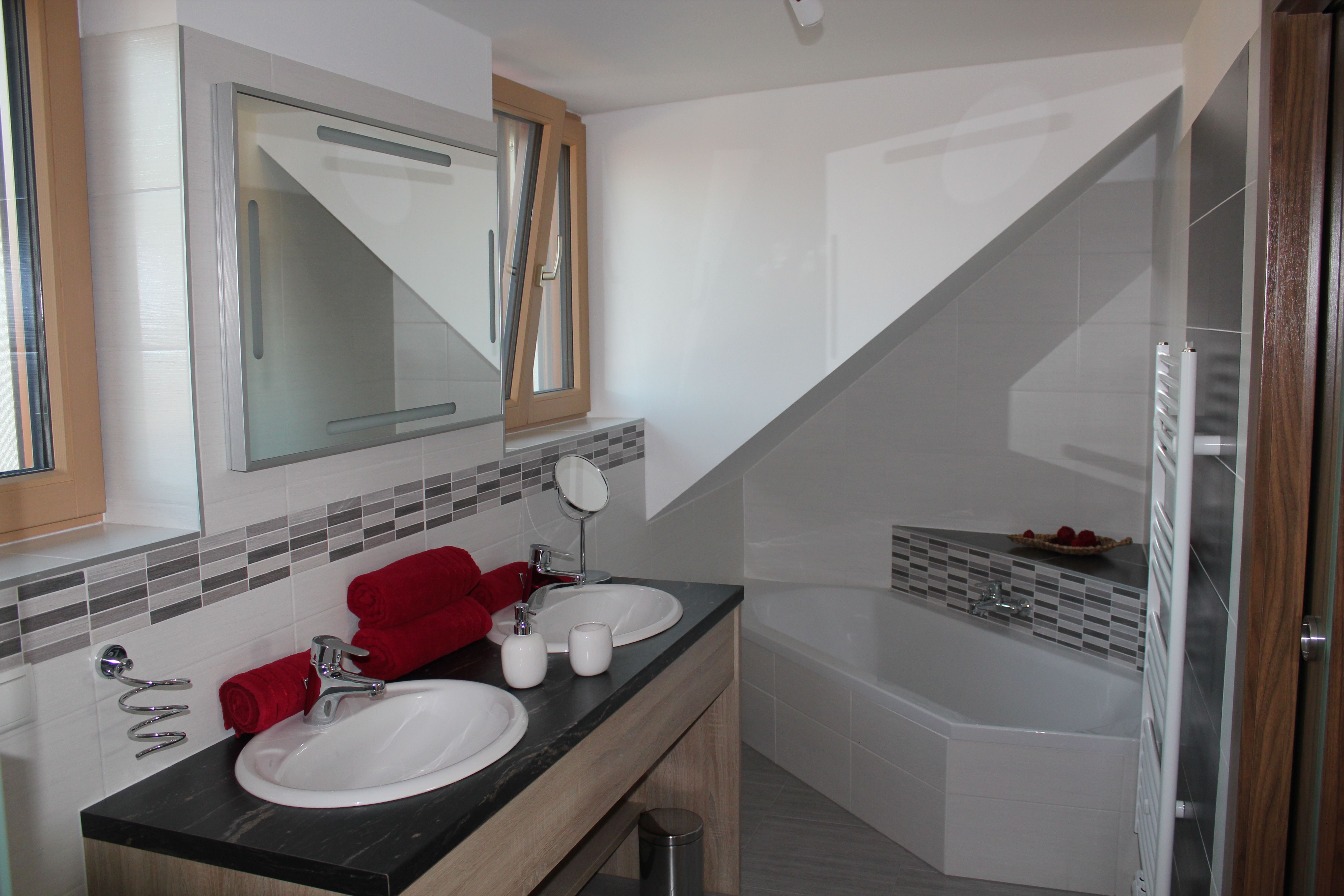 Moderná kúpeľňa s dvojitým umývadlom, vaňou a červenými uterákmi.