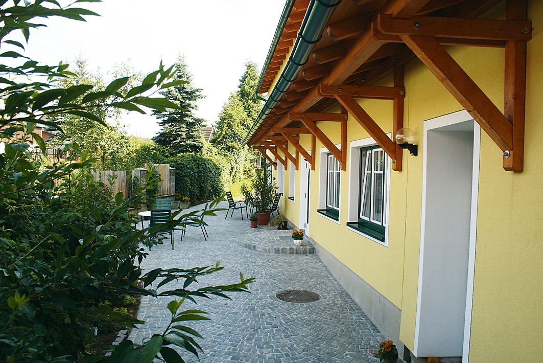 Vydláždený dvor so žltou budovou a záhradným nábytkom.