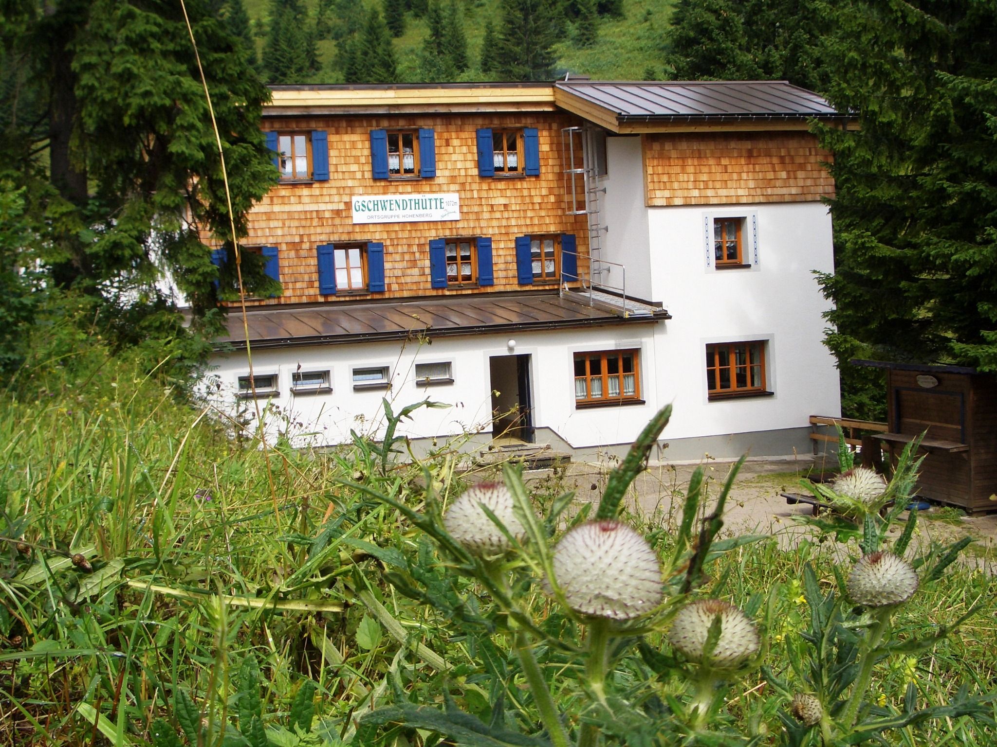 Gschwendthütte v Hohenbergu, obklopená zelenou prírodou a stromami.
