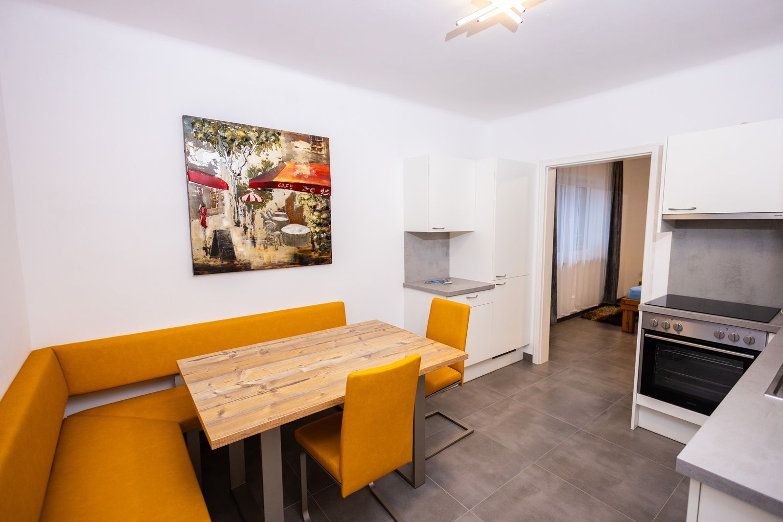 Moderná kuchyňa so žltou rohovou lavicou, dreveným stolom a umeleckým dielom na stene.