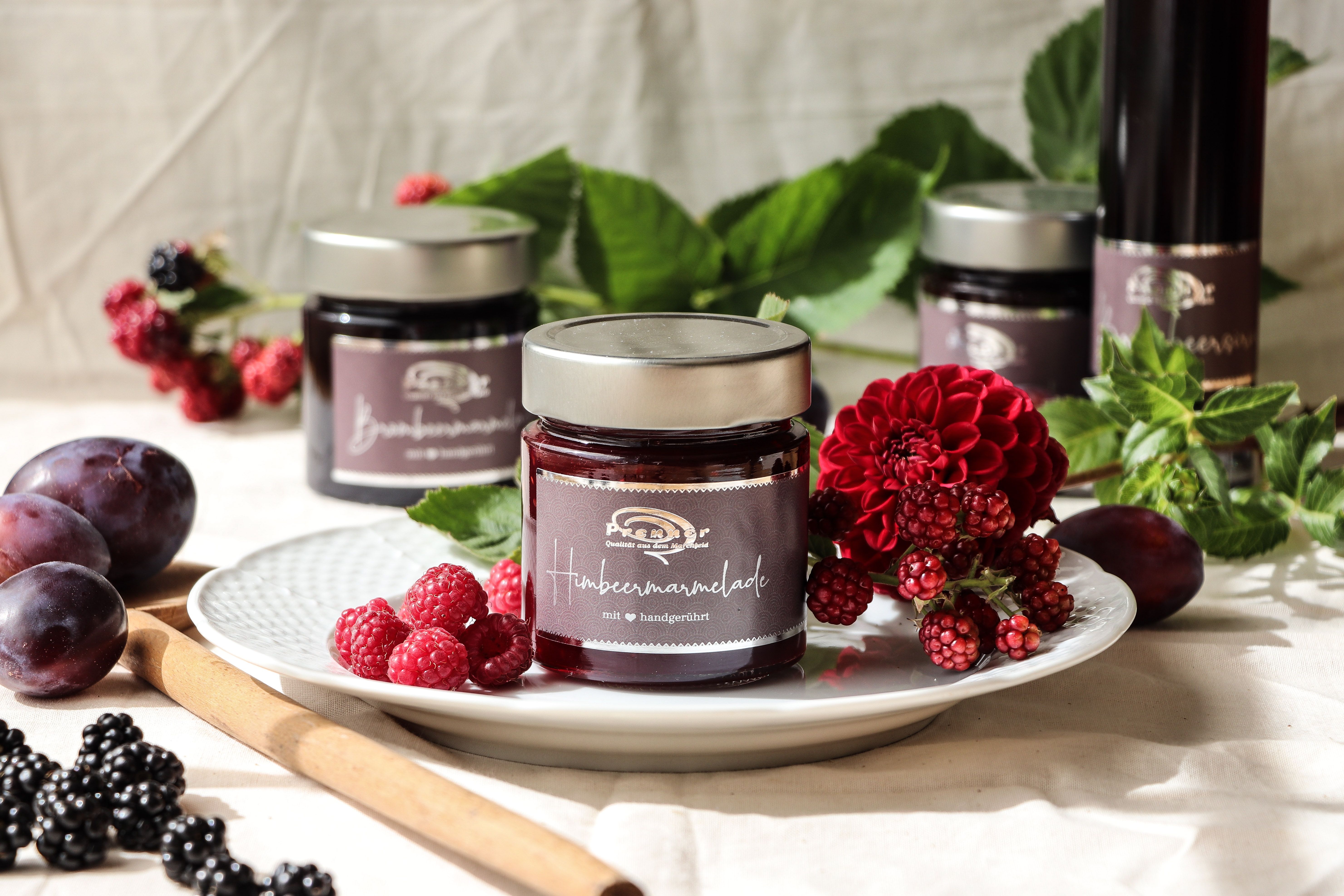 Pohár malinového džemu na tanieri zdobenom čerstvými bobuľami a kvetmi.