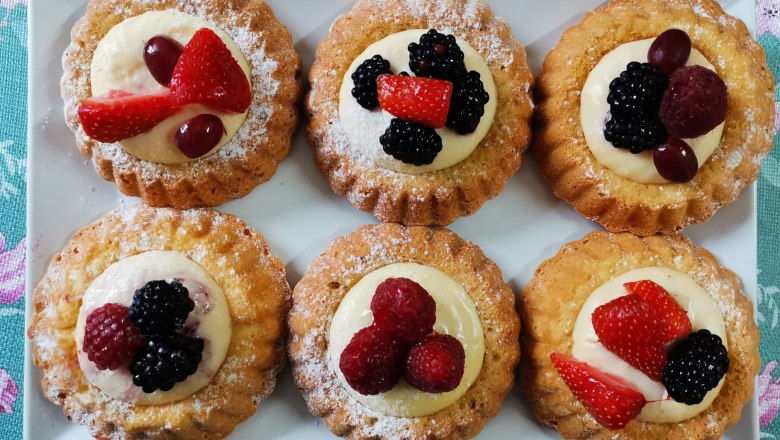 &Scaron;esť mal&yacute;ch ovocn&yacute;ch kol&aacute;čikov na bielom tanieri, zdoben&yacute;ch bobuľov&yacute;m ovoc&iacute;m a smotanou.