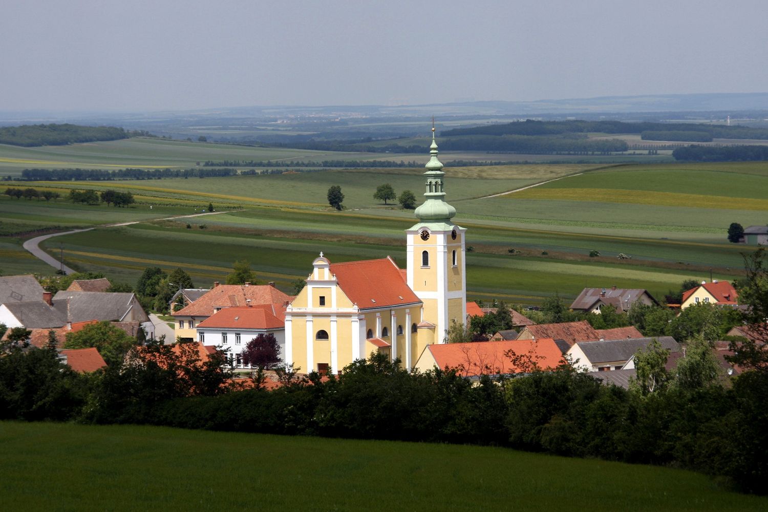 Pohľad na kostol v Ottenthale s okolitými domami a rozľahlými poľami v pozadí.