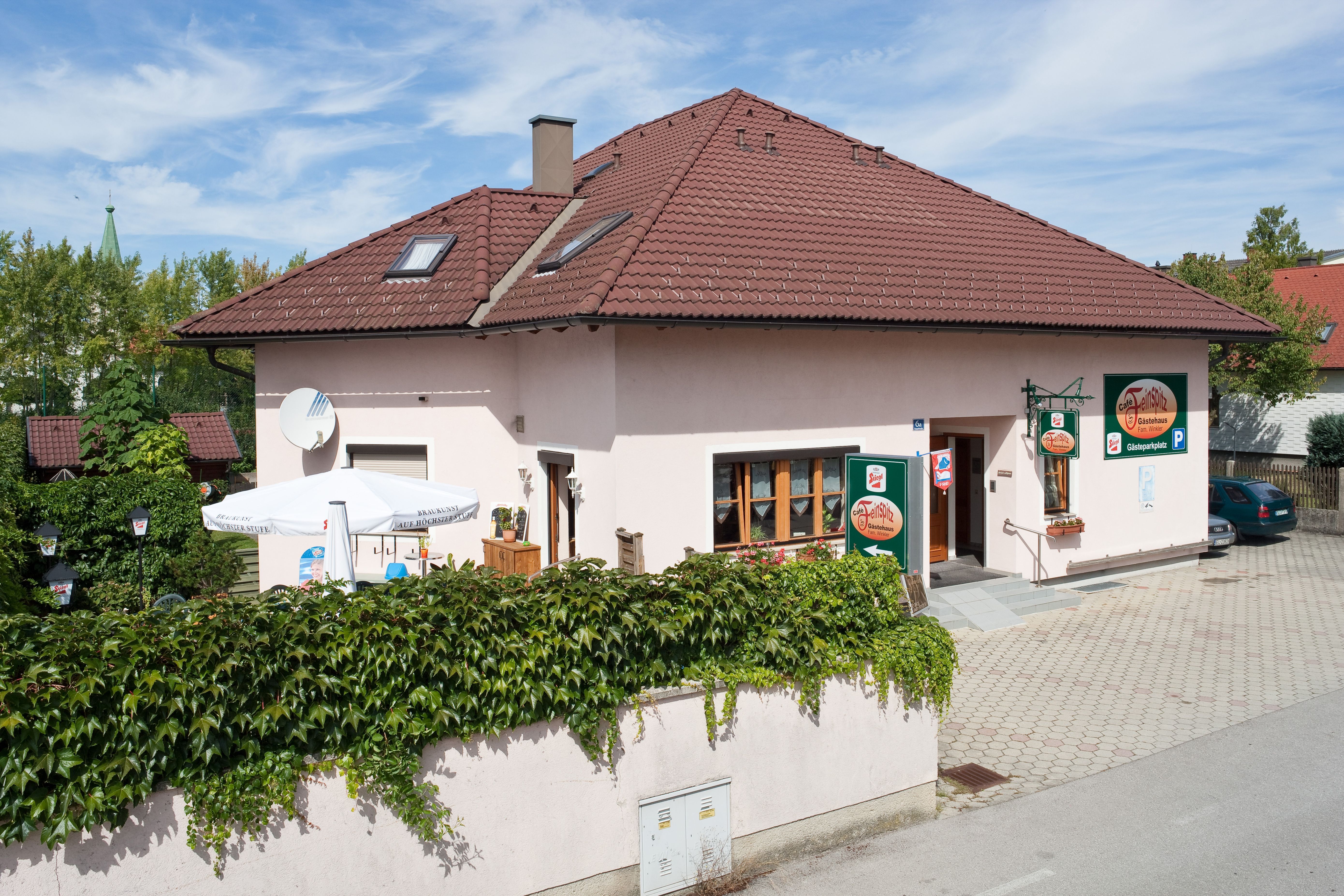 Penzión s červenou strechou a terasou, obklopený zelenou vegetáciou.