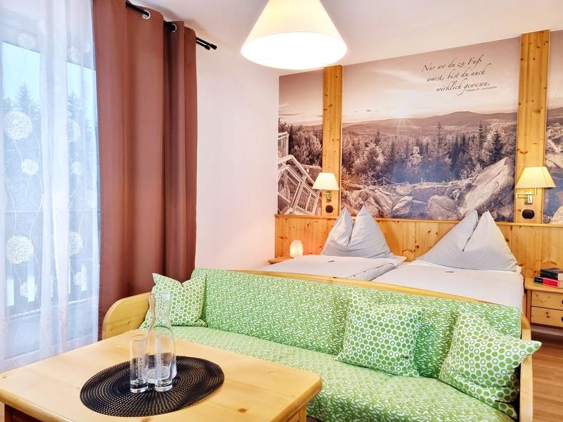 Útulná dvojlôžková izba s dvoma posteľami, zelenou pohovkou a veľkou nástennou maľbou krajiny.