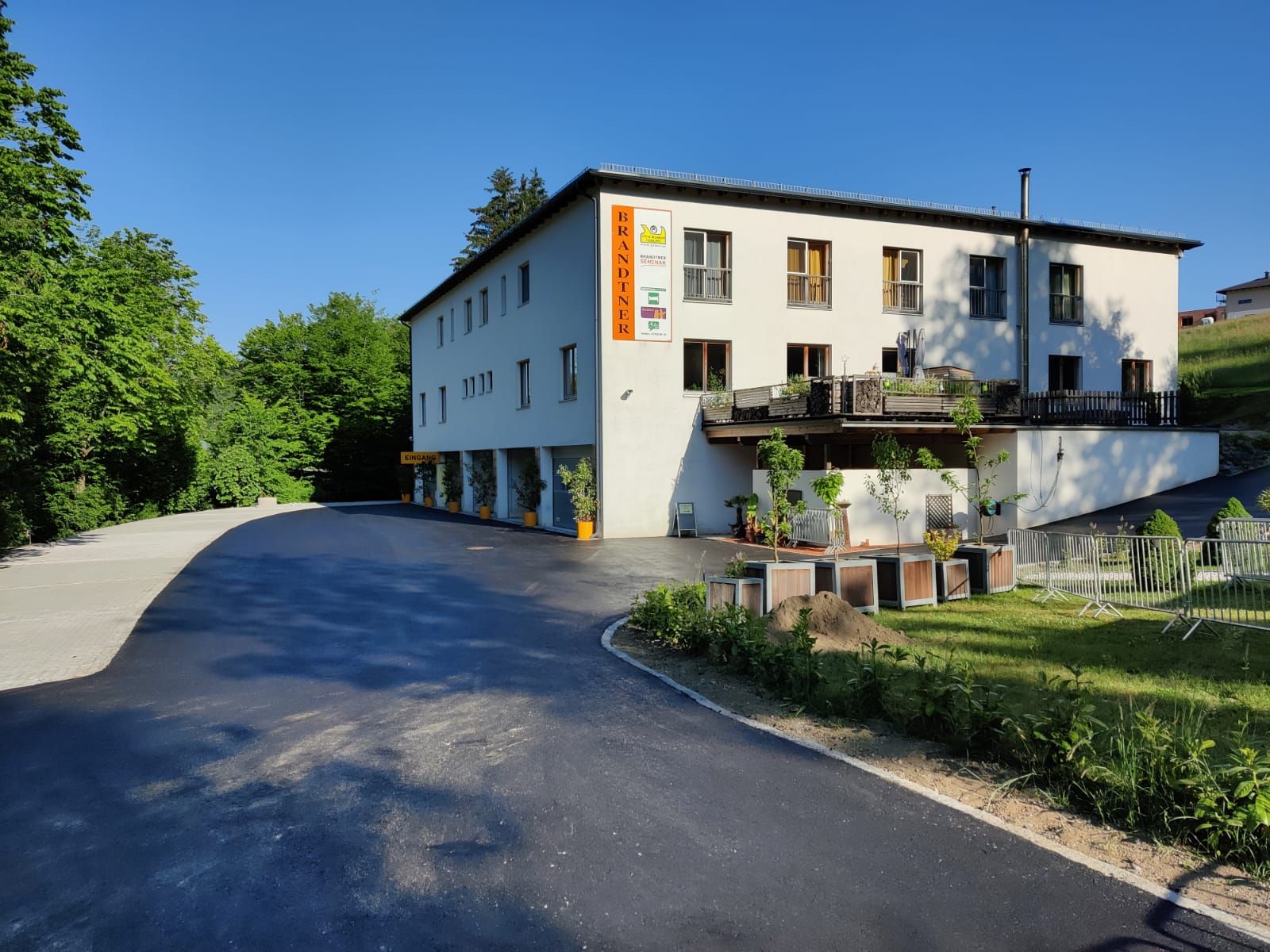 Budova s nápisom "Brandtner", obklopená stromami a parkoviskom.