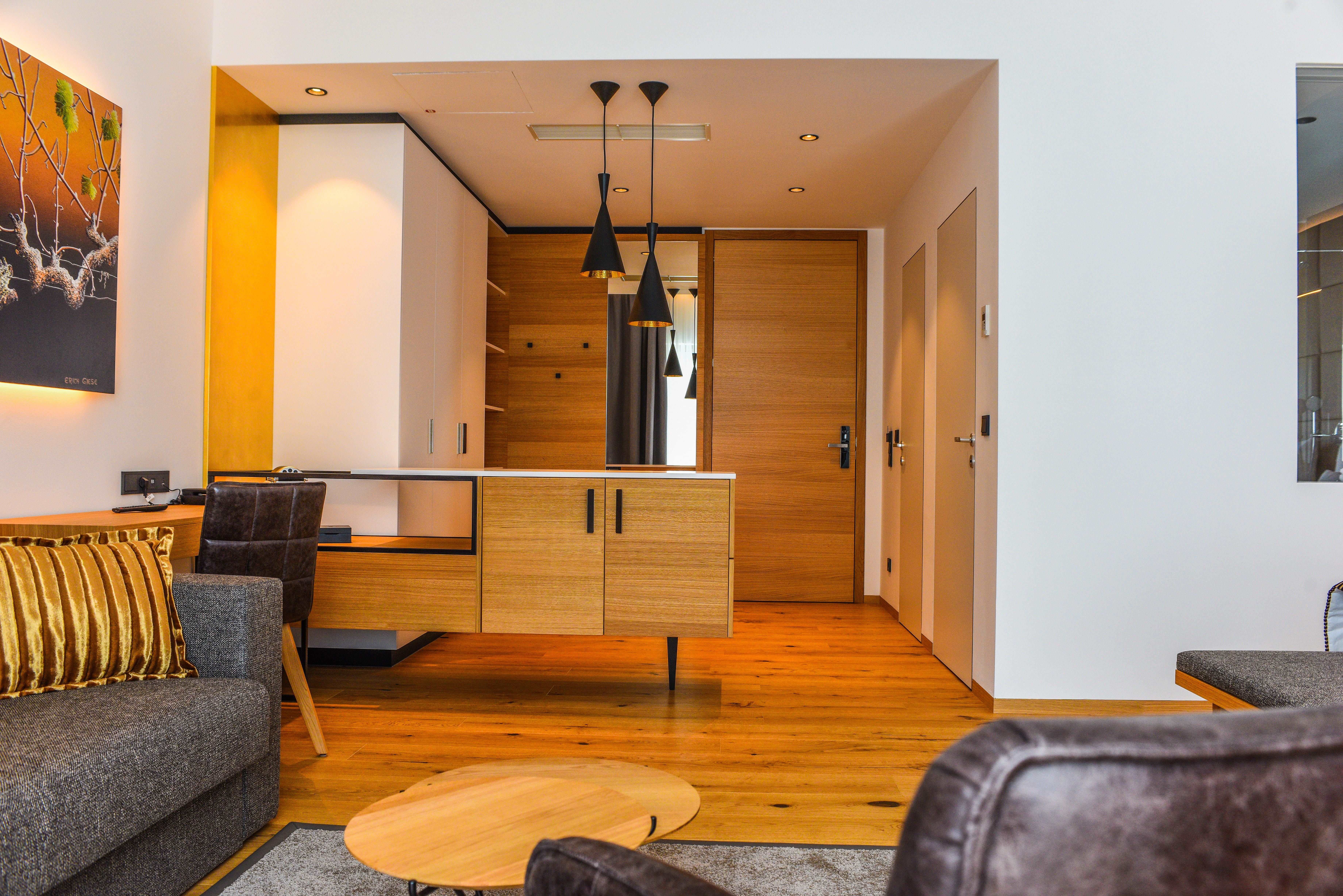 Pohľad do interiéru moderného hotelového apartmánu s drevenou podlahou, sivou pohovkou a dreveným stolom.